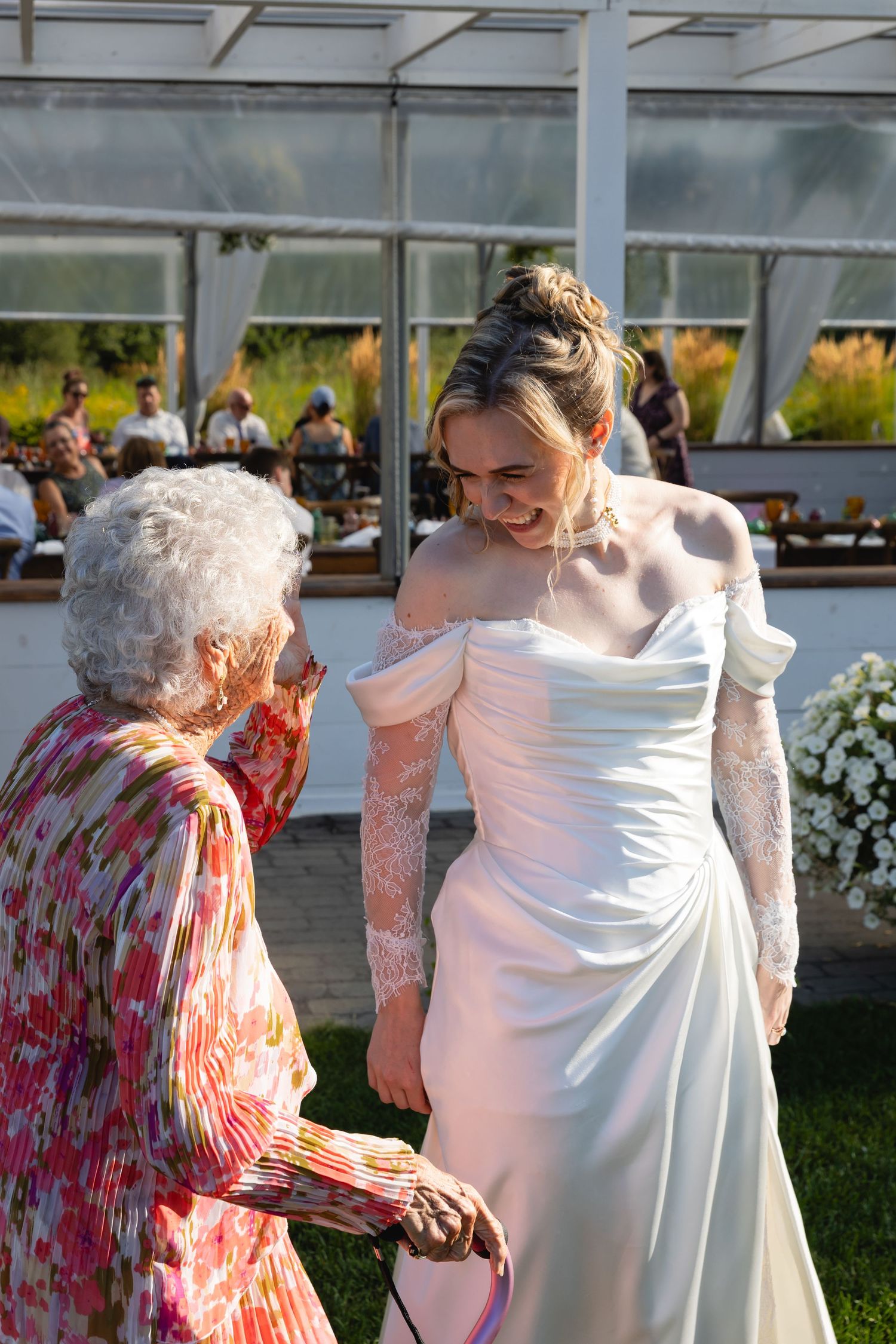 Wedding guests in formal attire gather outdoors under a white tent during a daytime celebration.
