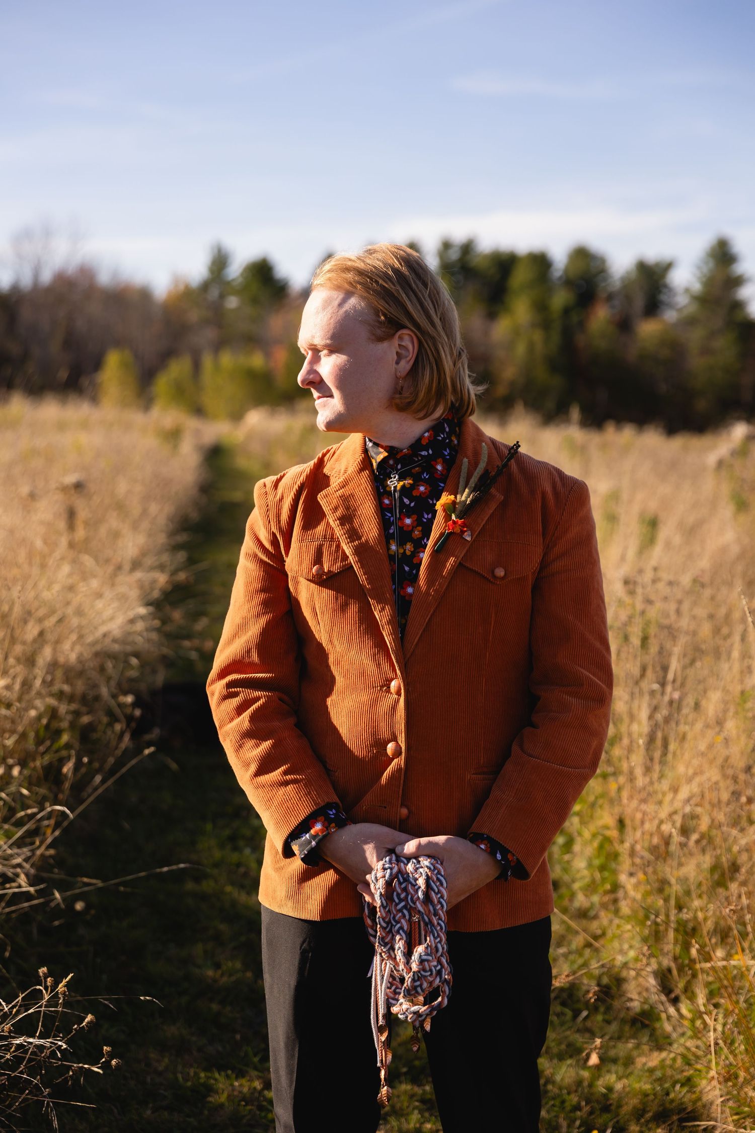 A person in a brown corduroy jacket stands in a golden autumn field during sunset.