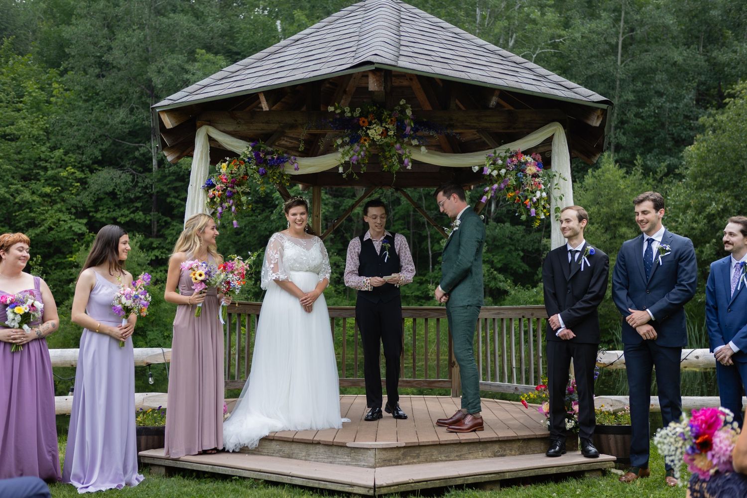 Wedding party stands on a decorated gazebo during an outdoor ceremony.