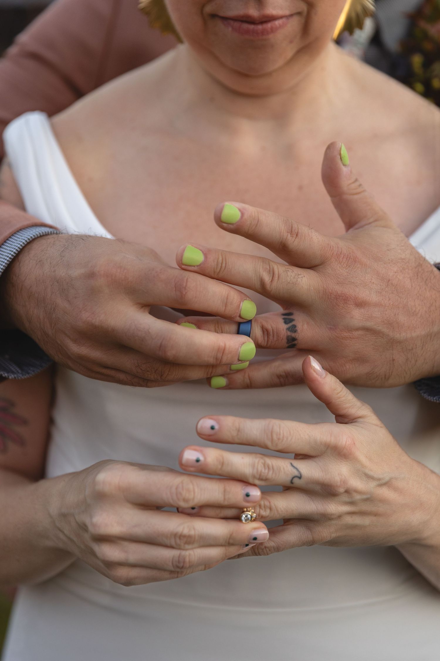 Hands with lime green and pink nail polish show off wedding rings.