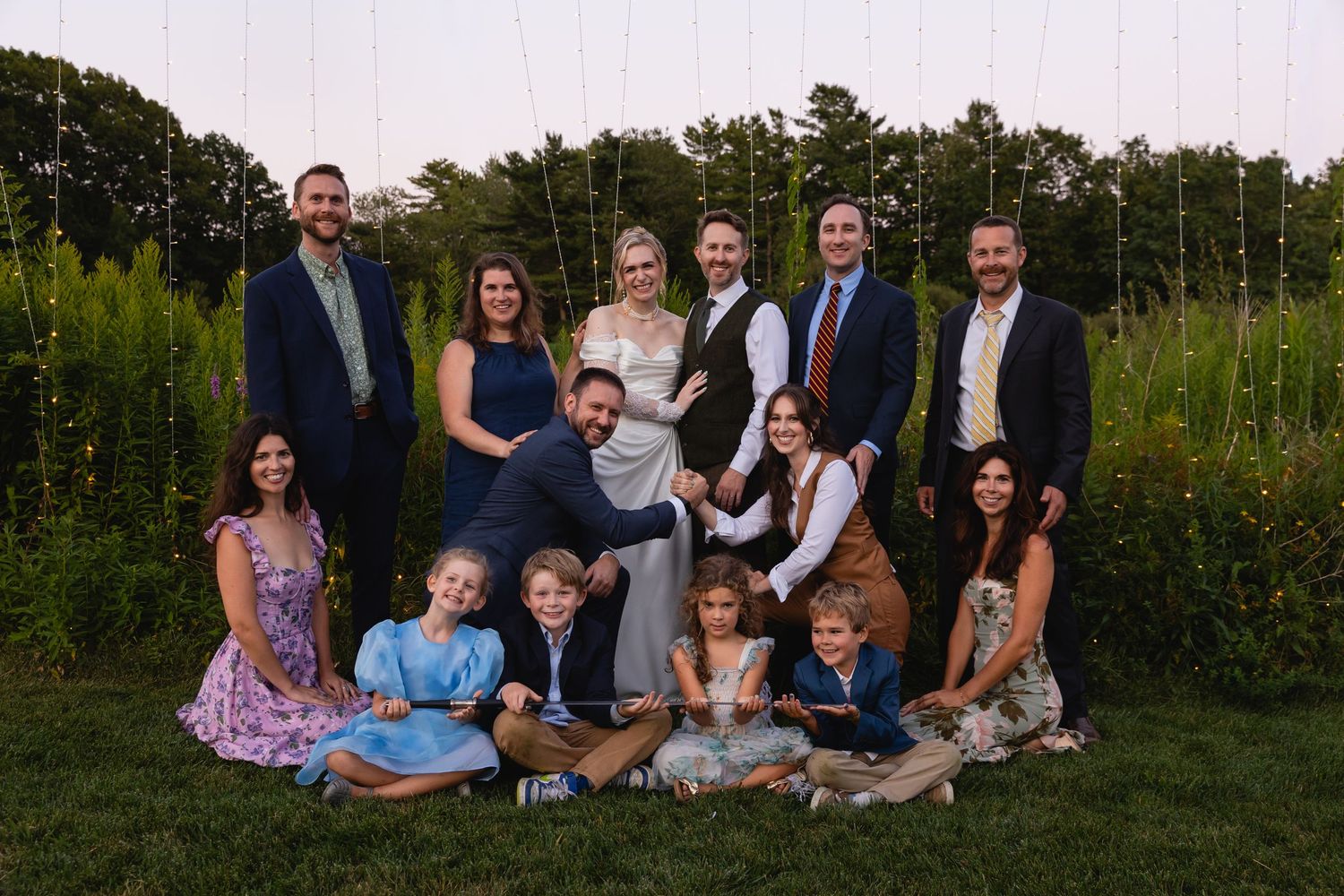 A group of people sitting and standing together for outdoor family portraits in a lush garden setting at sunset.