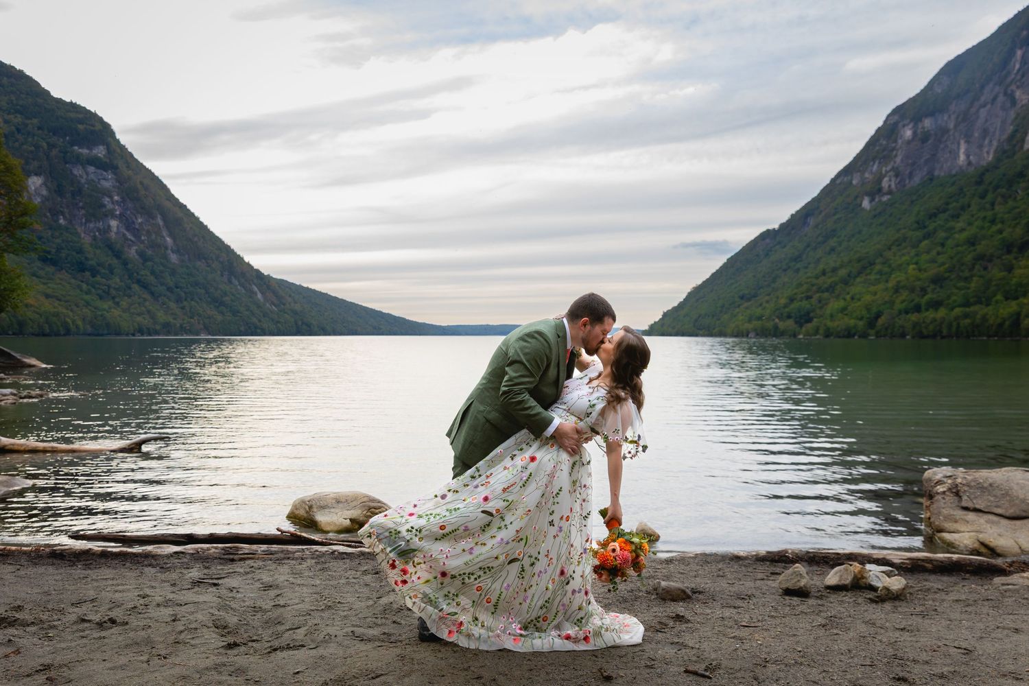 A romantic couple shares an intimate moment by a serene fjord surrounded by majestic mountains and calm waters.