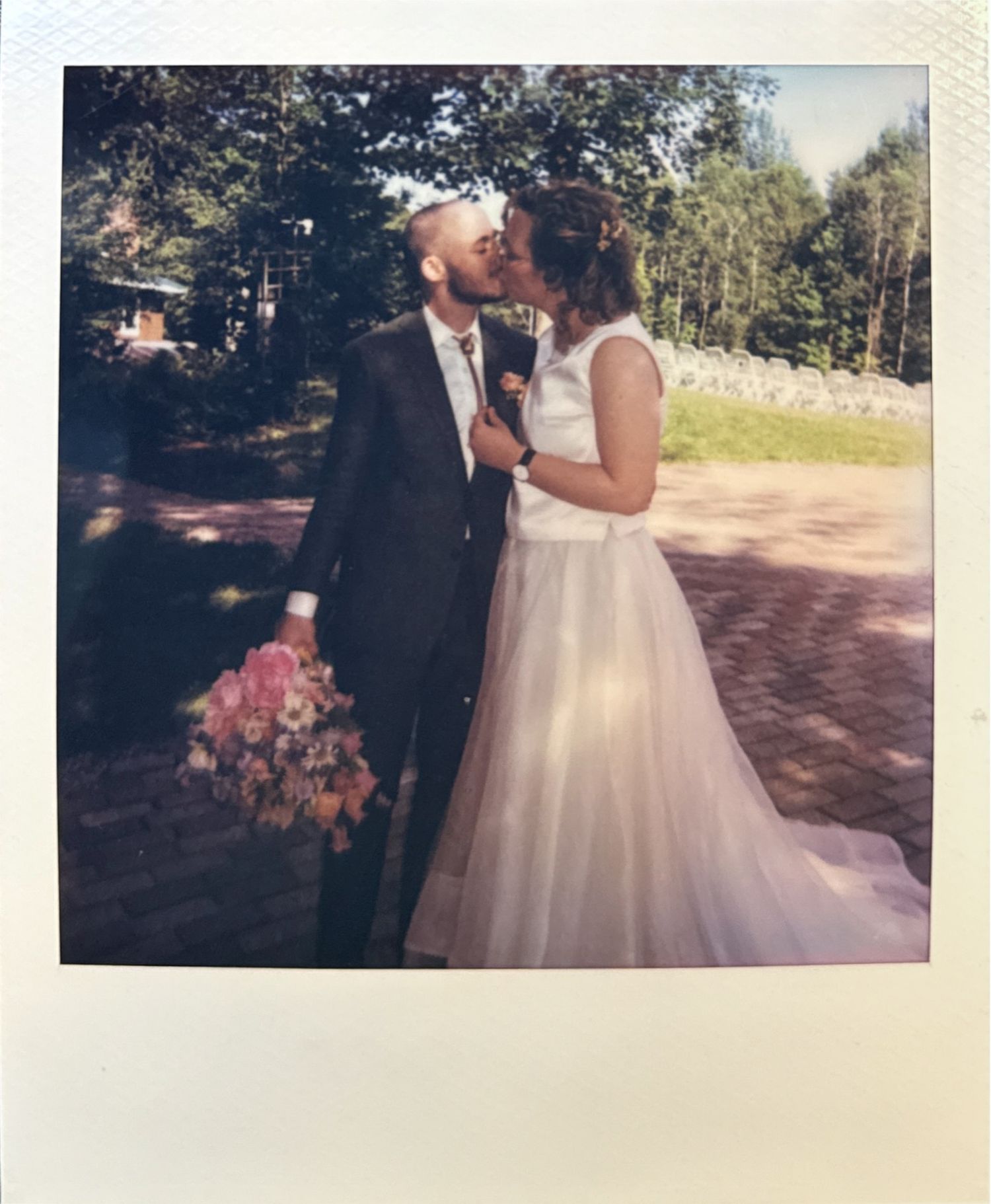A couple shares a romantic moment during their outdoor wedding ceremony in a sunlit forest setting.