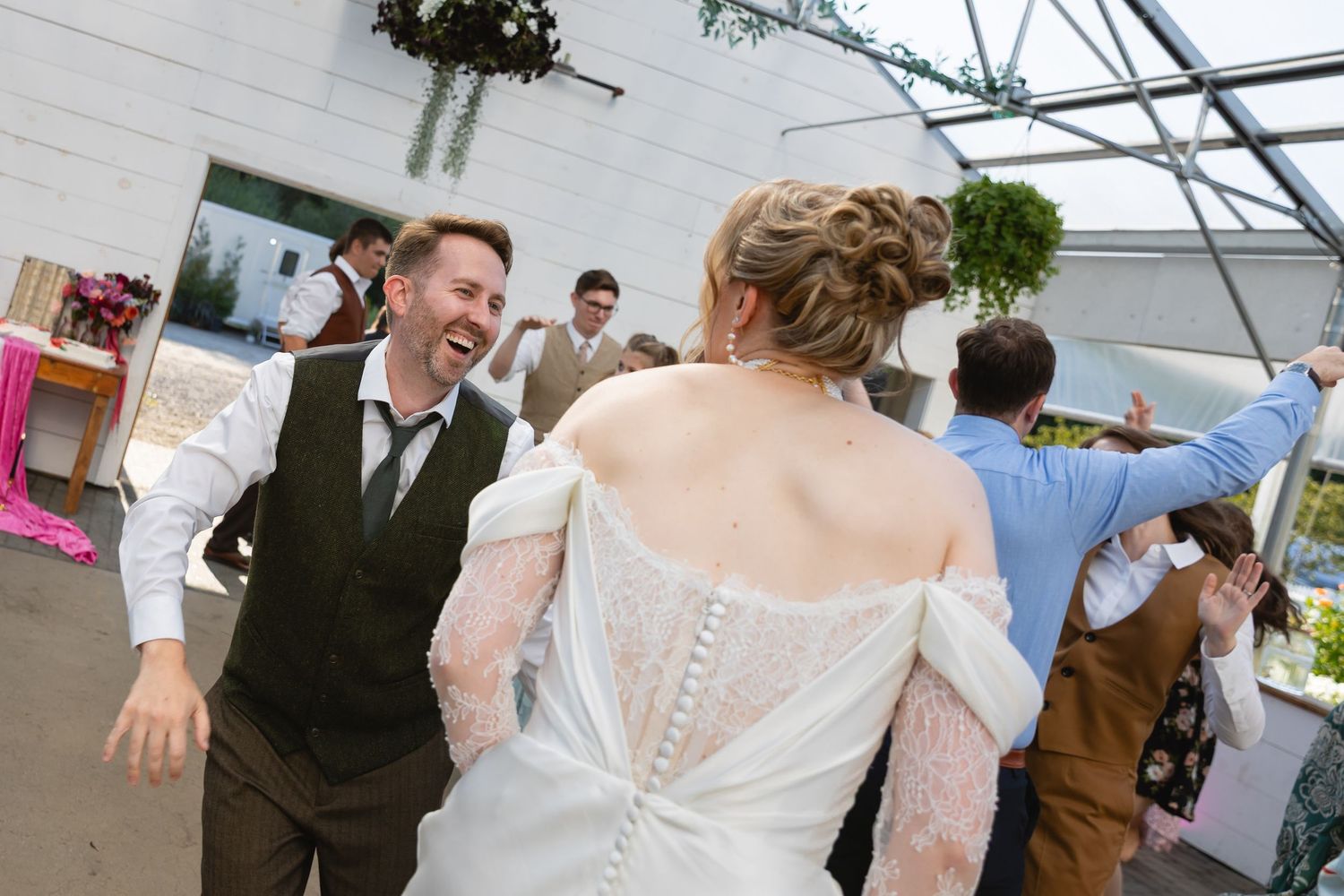 A wedding reception scene in a white tent with guests mingling and dancing together on a sunny day.
