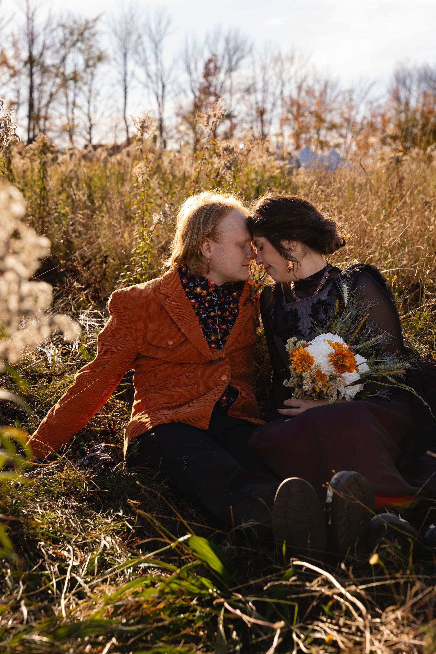 A couple shares a romantic moment while sitting together in a golden autumn field at sunset.