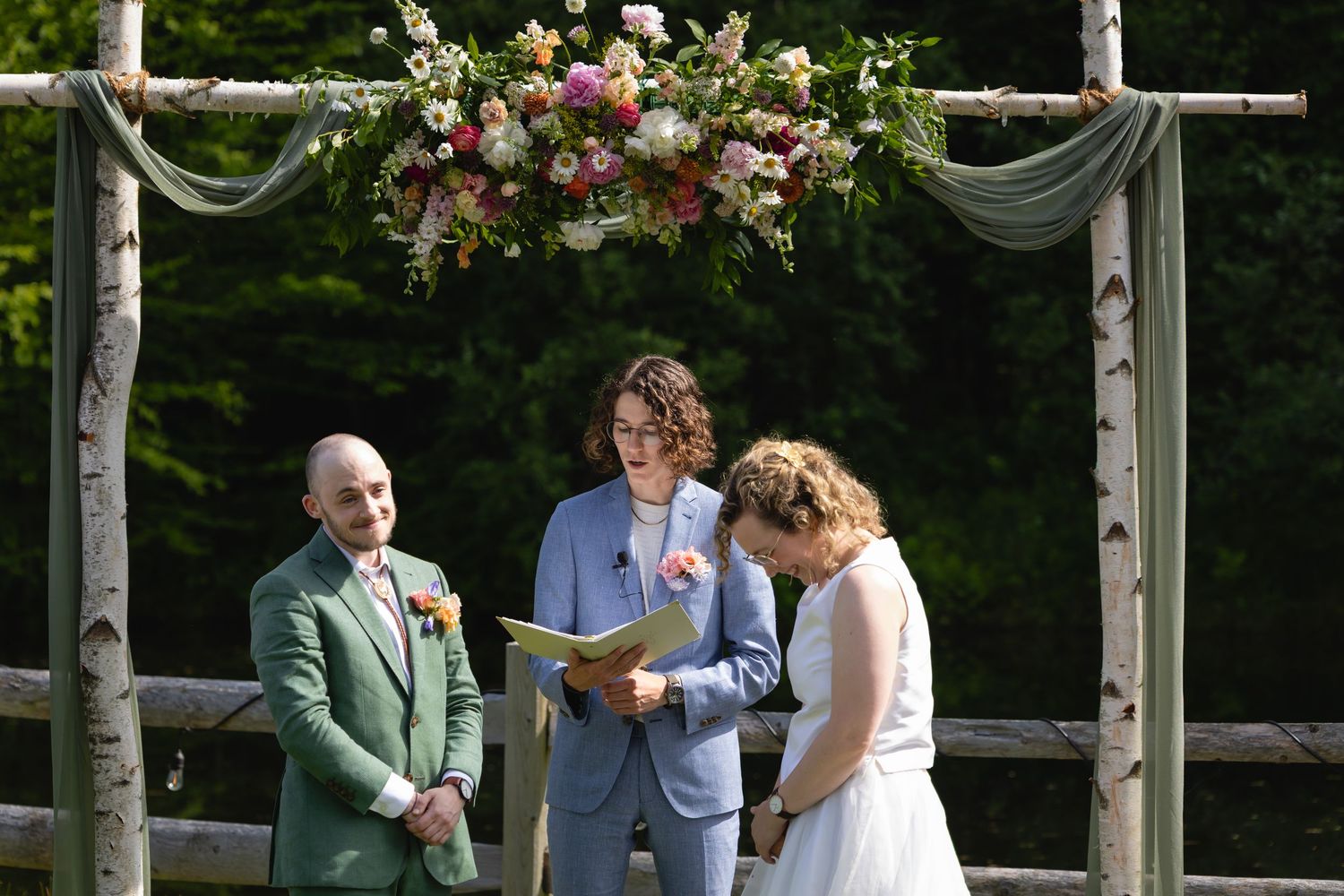 A couple shares an intimate moment during their outdoor garden wedding ceremony beneath a floral-adorned arbor.