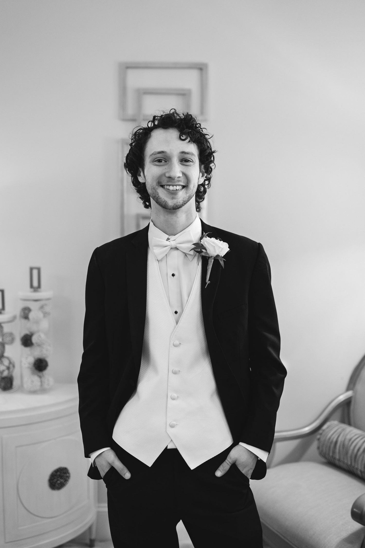 Black and white portrait of a groom in a tuxedo and white vest smiling at the camera on his wedding day.