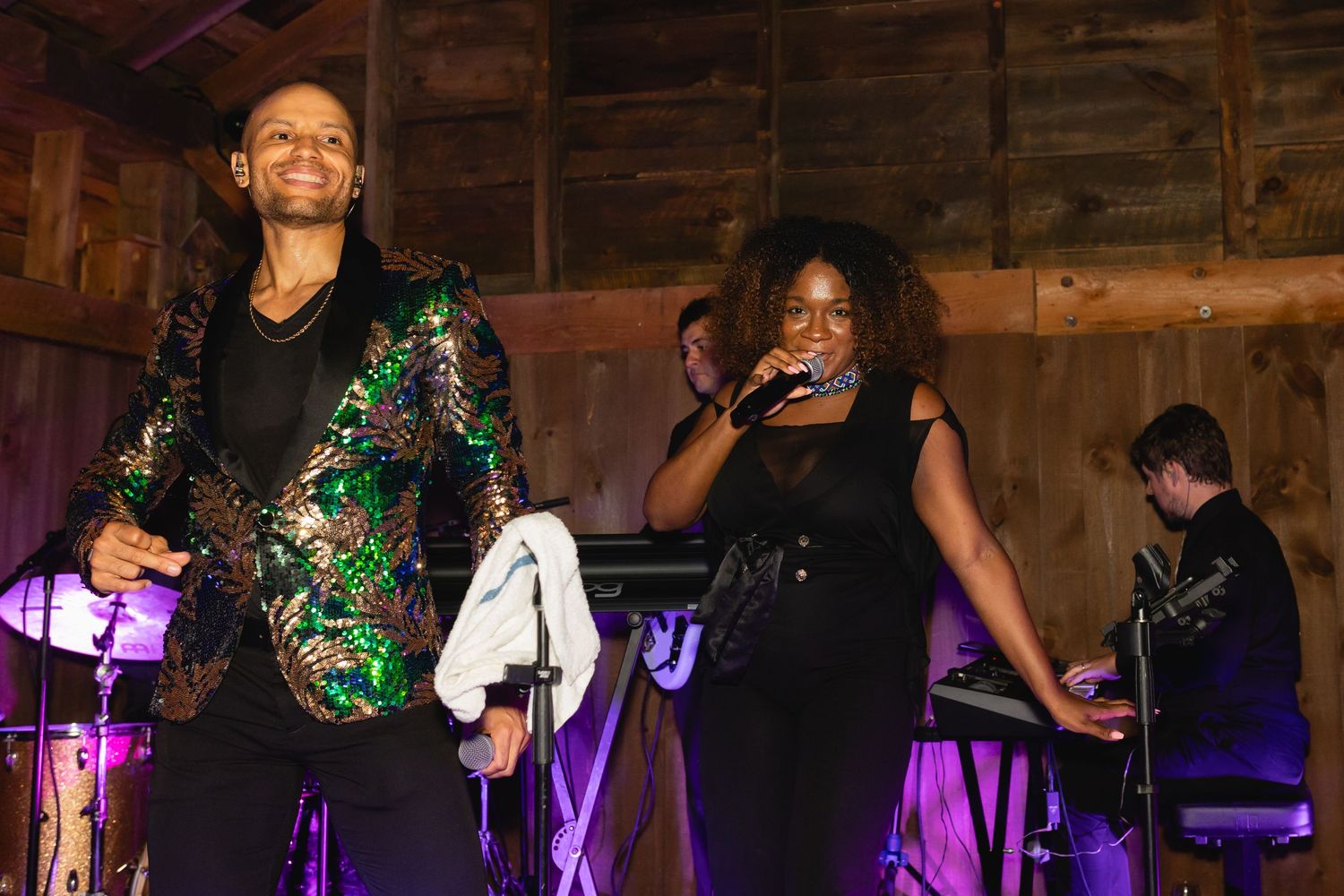 Musical performers on stage under purple lighting in a rustic wooden barn venue.