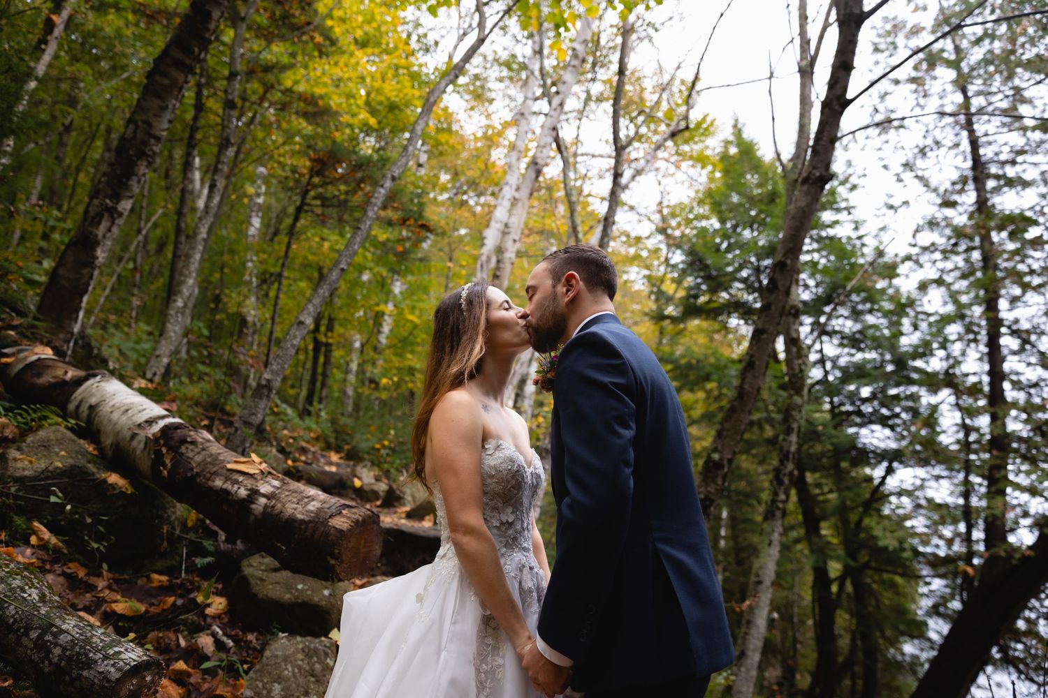 A romantic woodland wedding photo showing a couple embracing among fall foliage and birch trees.