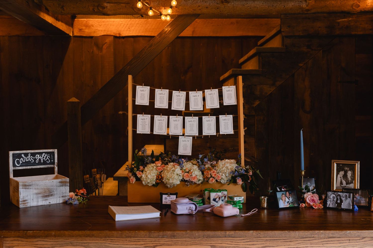 A rustic display table at a wedding features floral arrangements, hanging papers, and decor items in warm lighting.