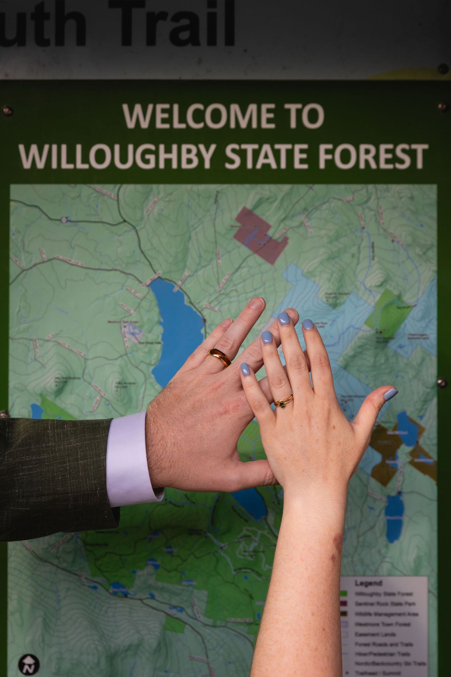 Newlyweds display wedding rings on Willoughby State Forest trail map sign.