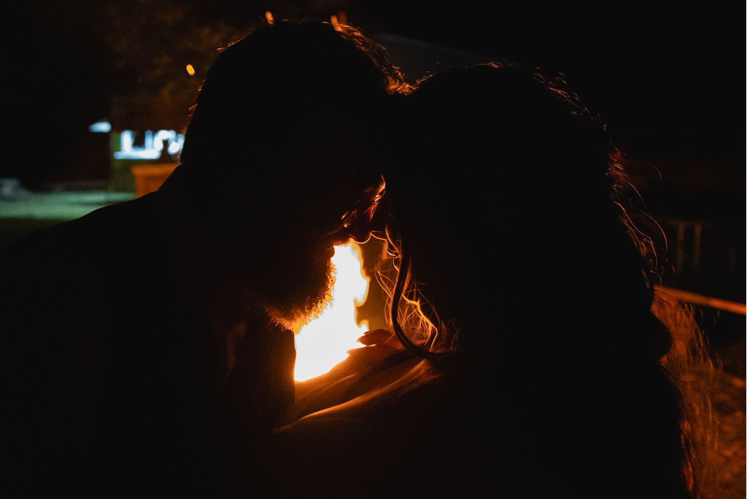 A silhouette of a couple illuminated by firelight in the darkness.