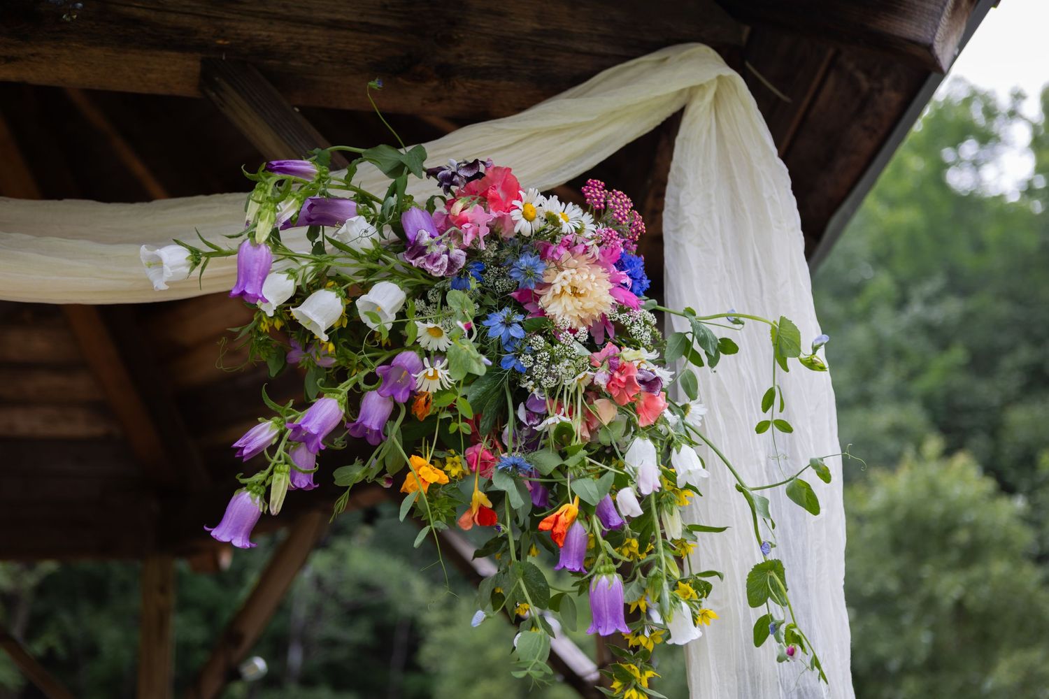 Colorful floral wedding decoration with purple and pink flowers draped with white fabric.