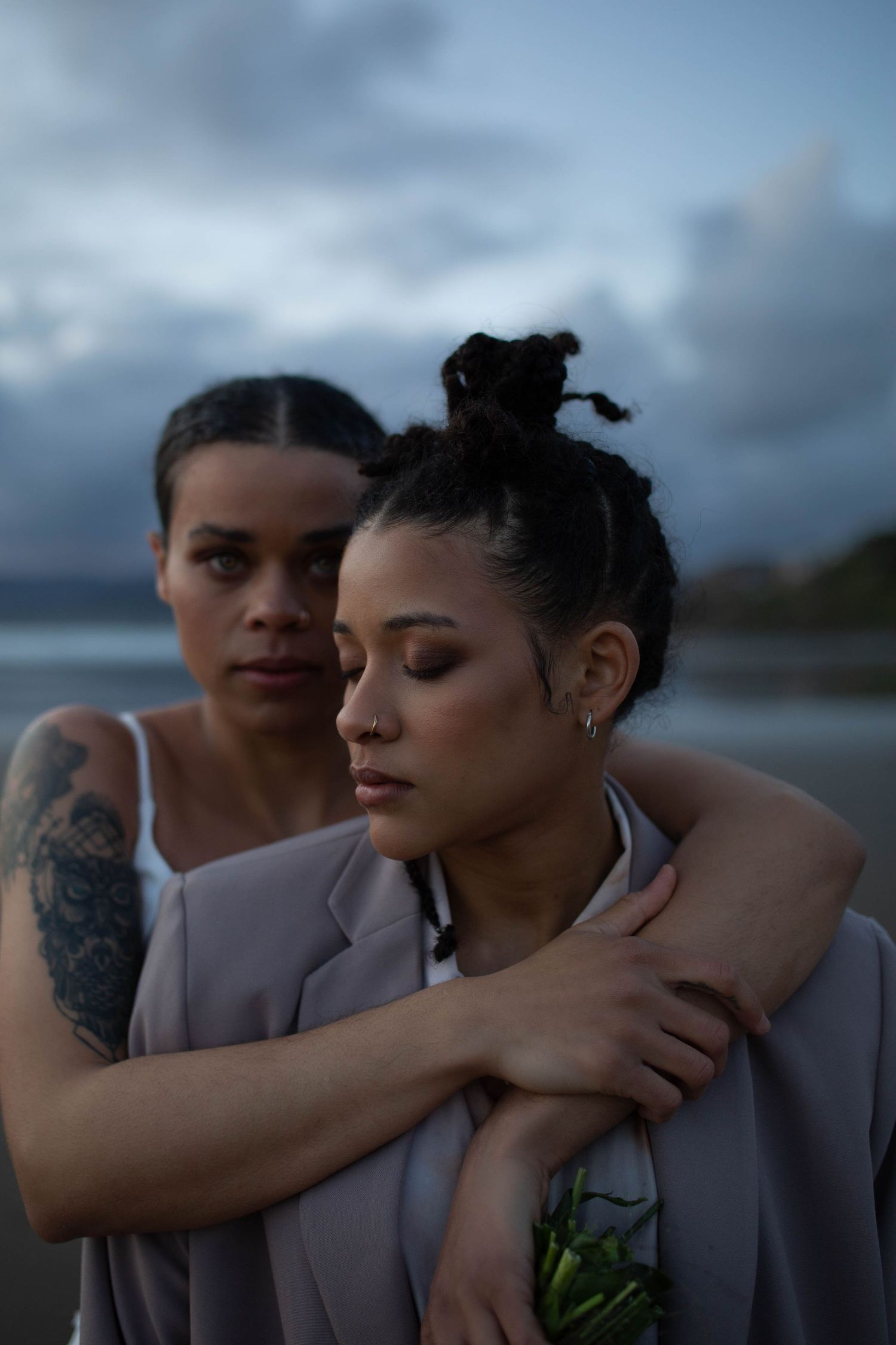 A close emotional portrait of a couple in matching grey blazers against a cloudy sky.