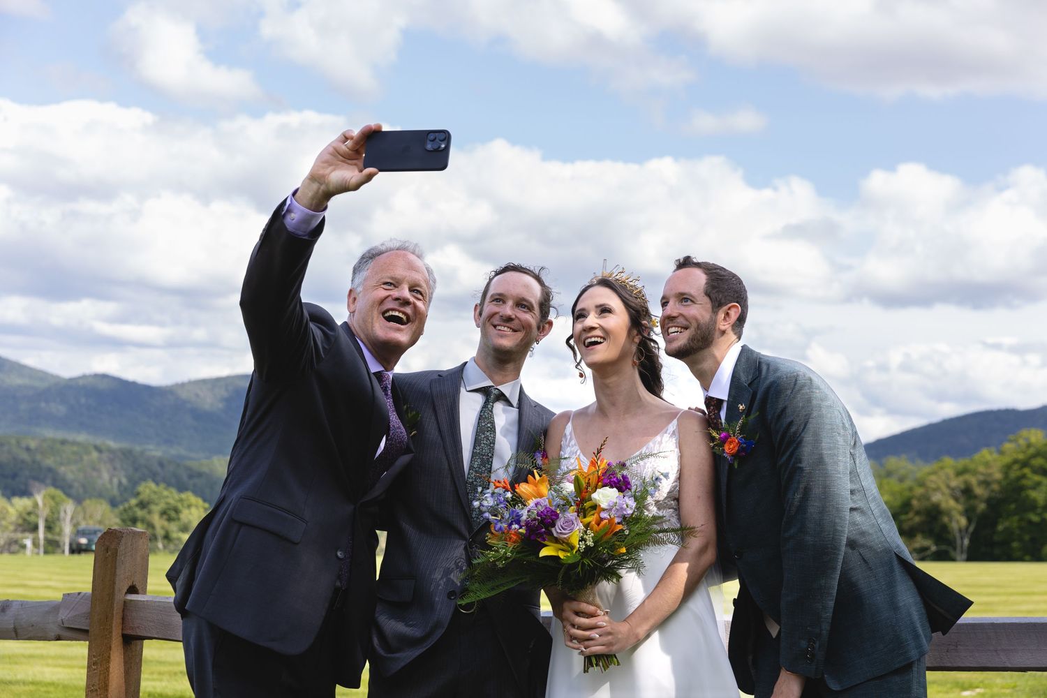 Group taking a selfie outdoors with mountain scenery and blue skies in the background.