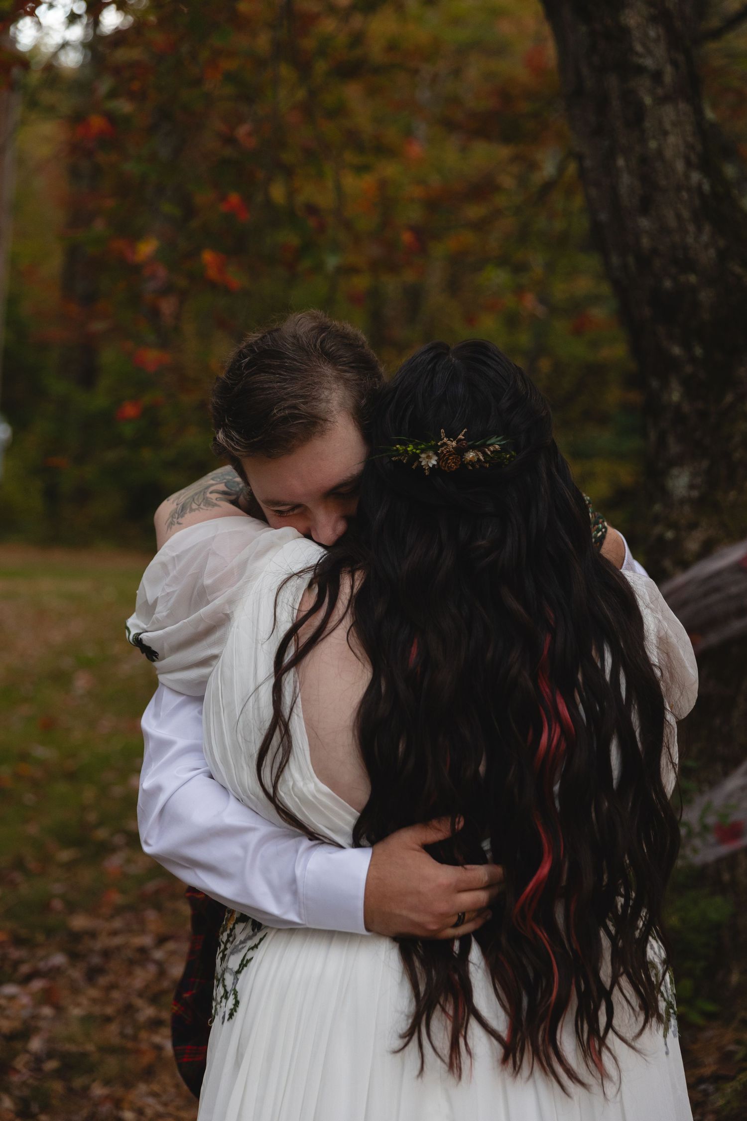 Bride and groom share an emotional embrace in an autumn forest, bride wearing floral crown and white gown.
