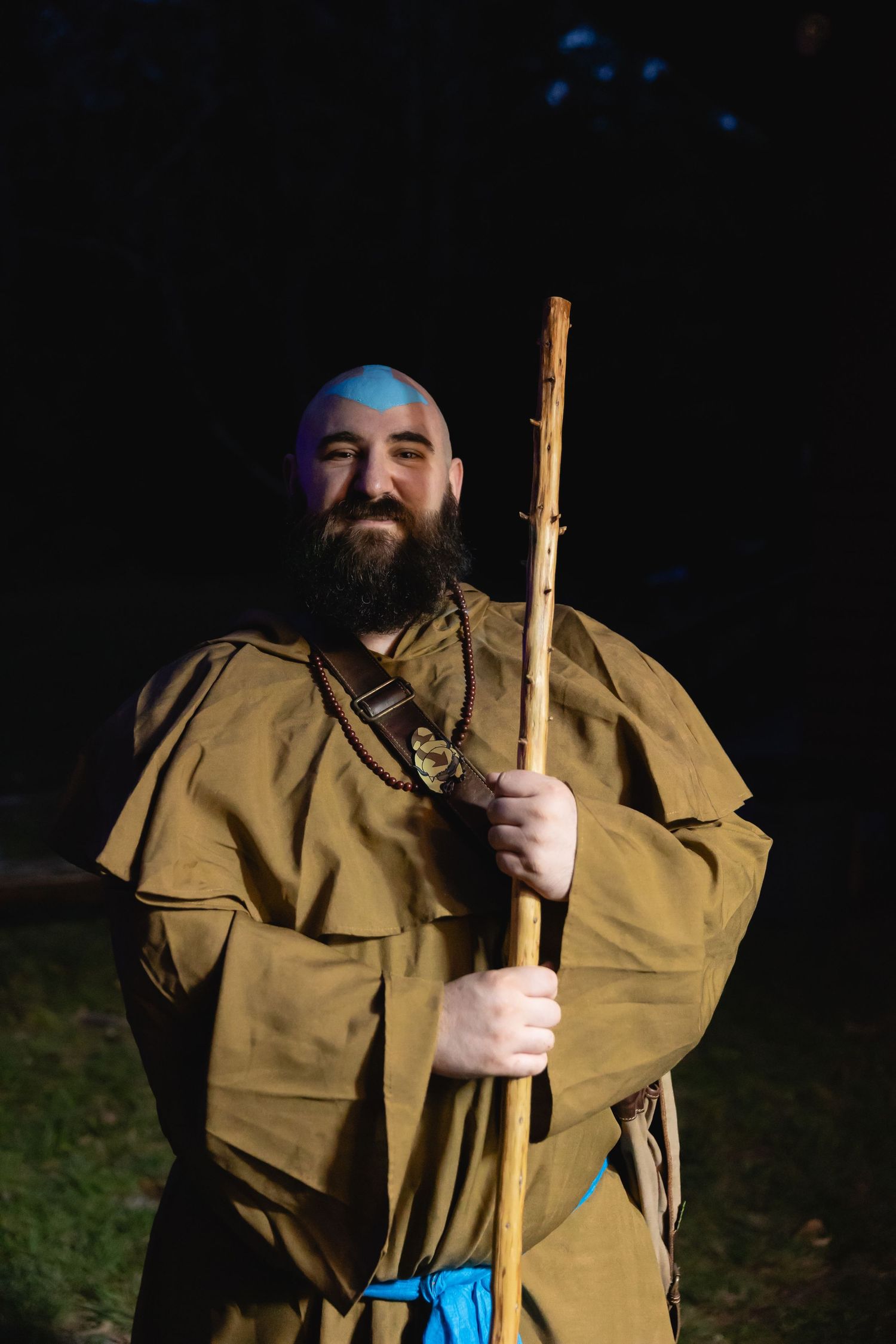 Bearded man in medieval costume holding a wooden staff with blue face paint at outdoor event.