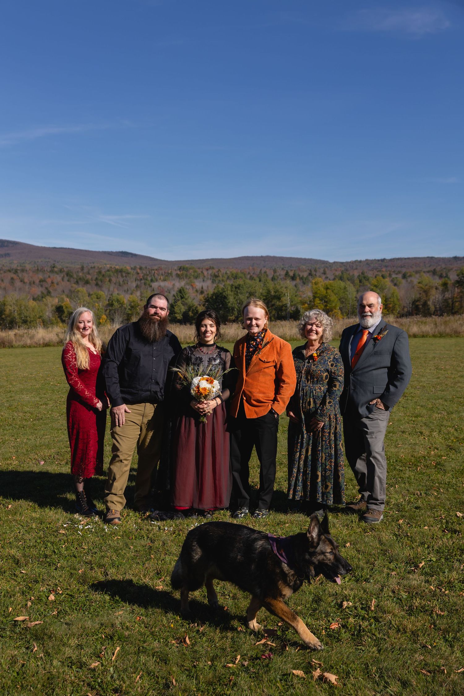 A group of people standing together in a sunny autumn field with mountains and fall foliage in the background.
