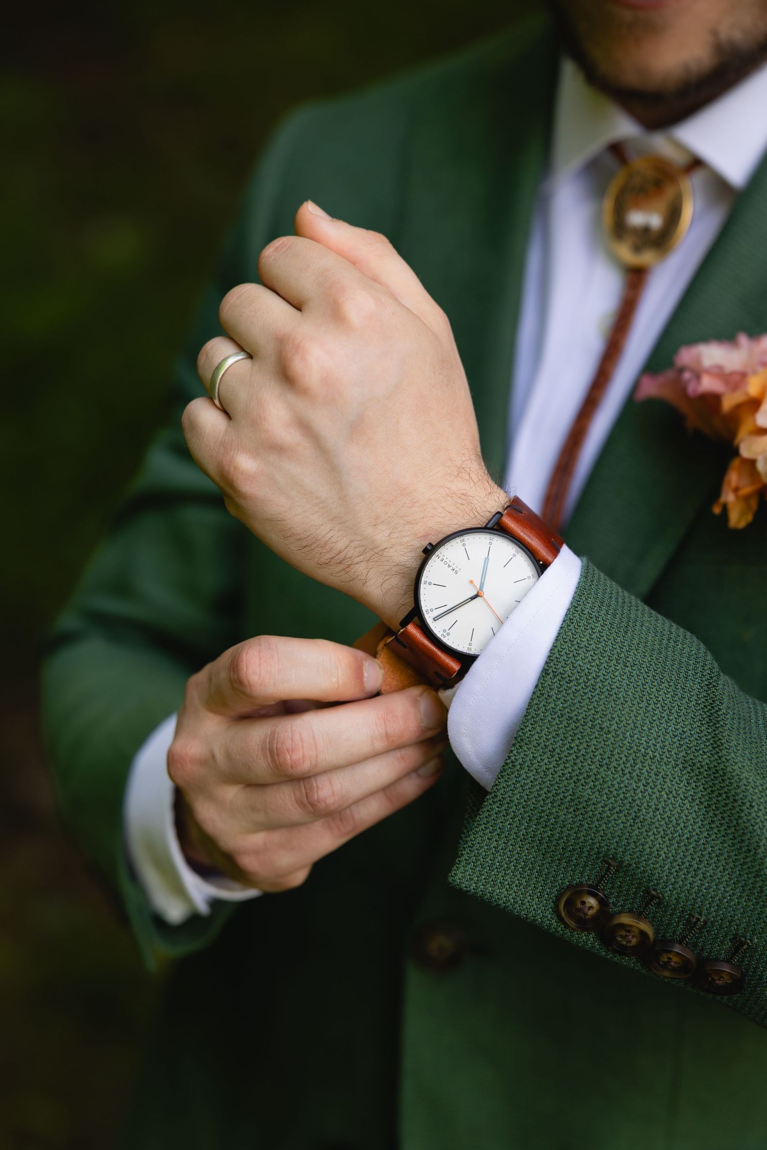 Close-up of a wristwatch with brown leather strap worn with an elegant green suit and white dress shirt.