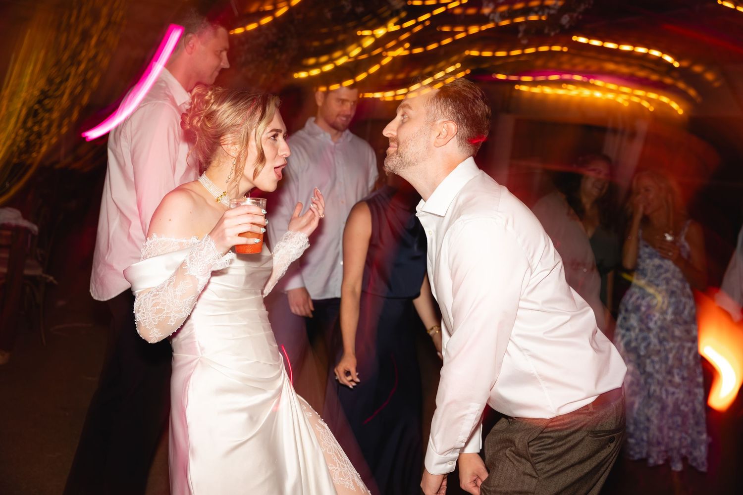 Dancers move energetically on a dimly lit dance floor illuminated by pink and orange lighting effects.