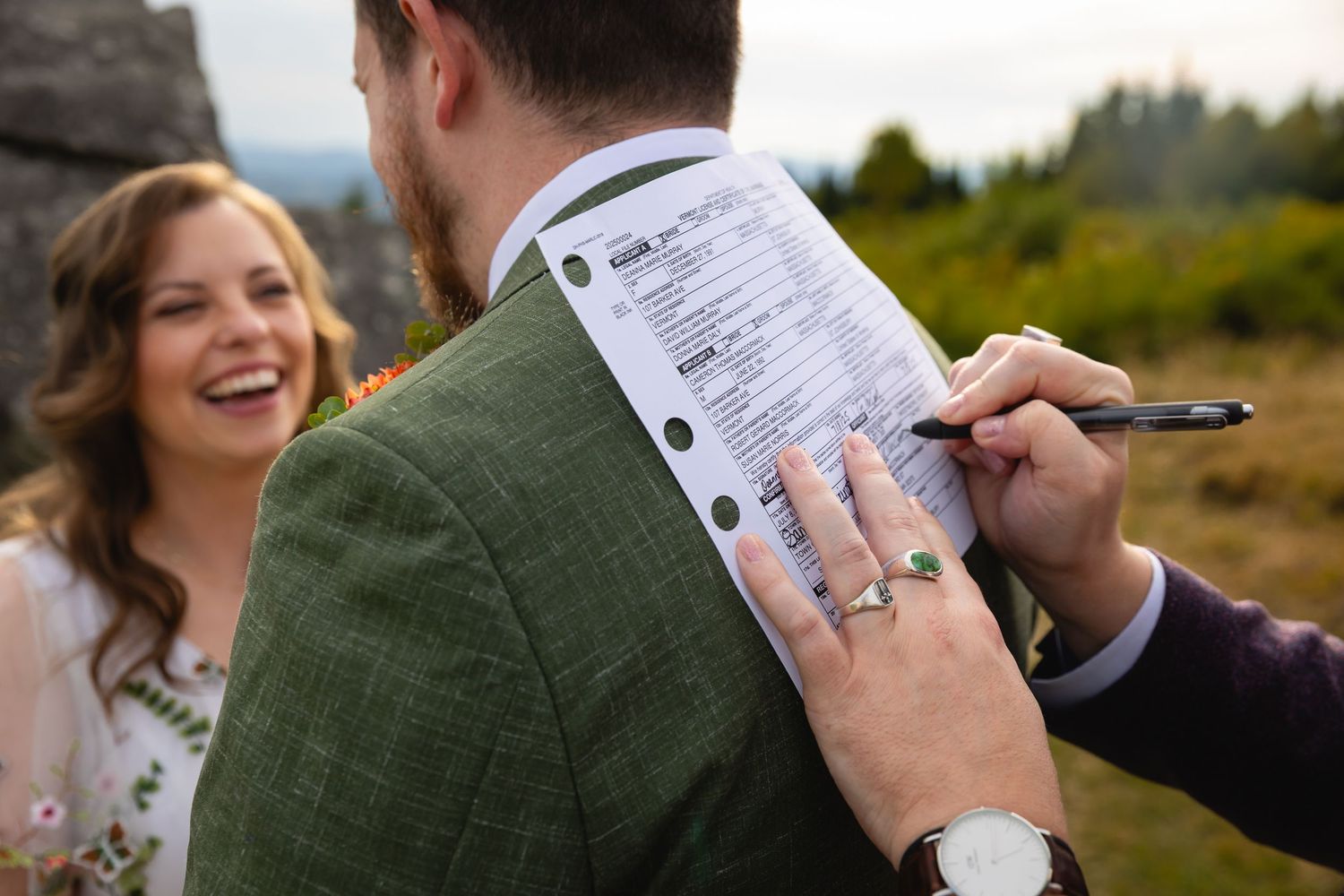 Couple signs marriage license together outdoors while sharing joyful laughter during wedding ceremony.