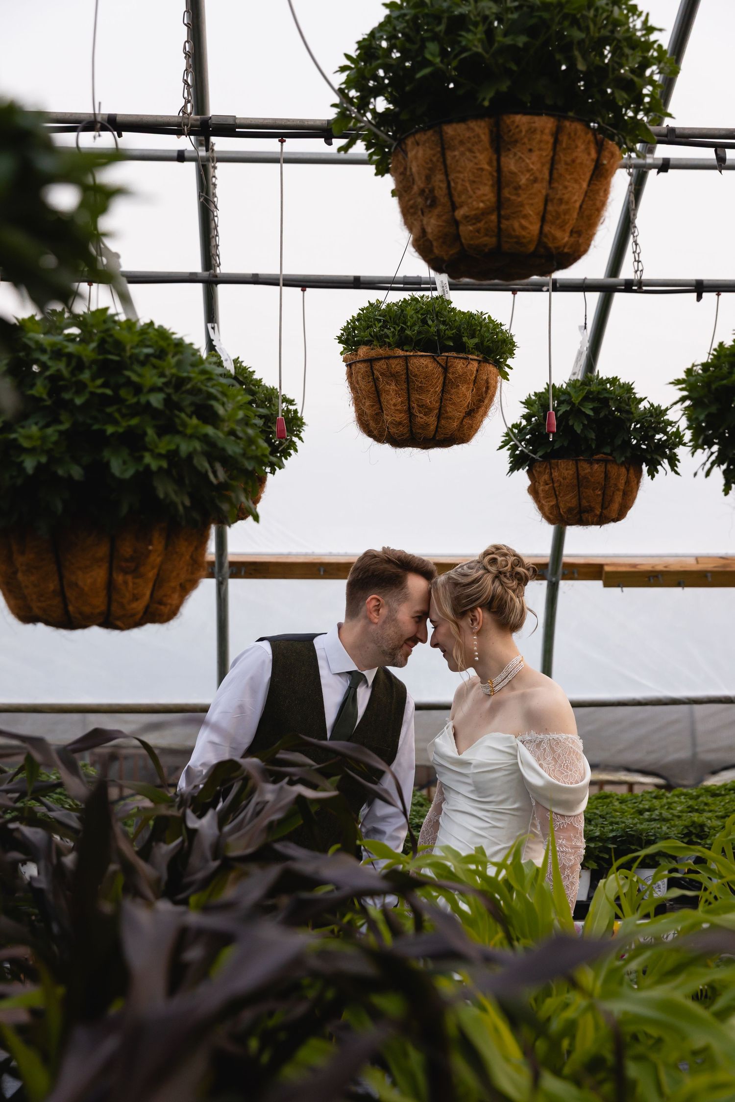 A romantic greenhouse wedding moment surrounded by hanging baskets and lush greenery.