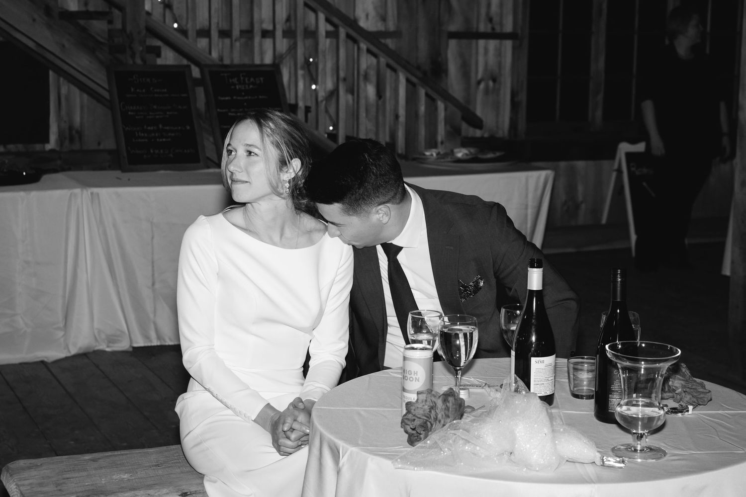 A couple in formal attire sits together at a table with drinks and white tablecloths in a black and white photograph.