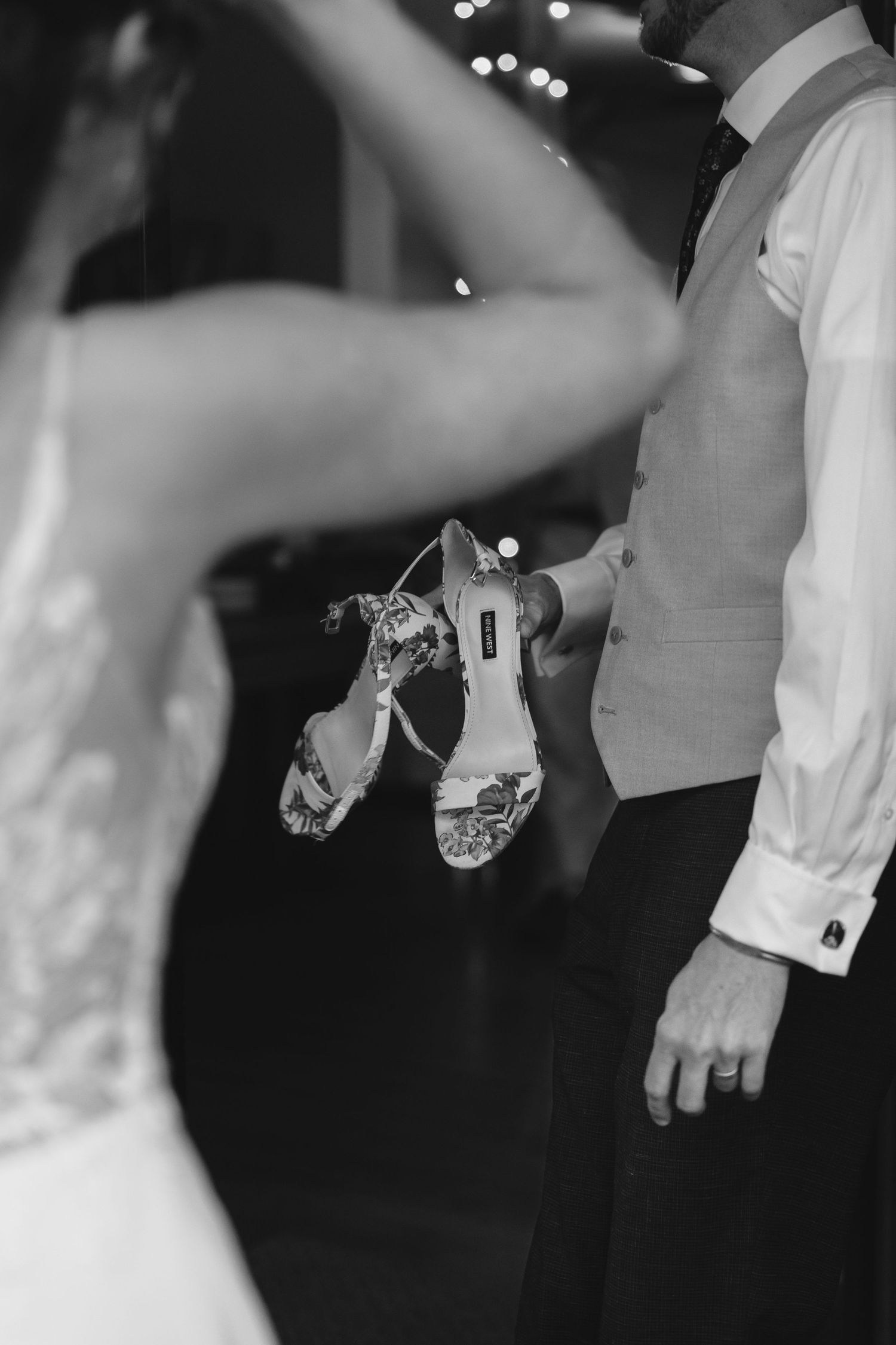 A black and white photo showing wedding shoes being held during a dance.