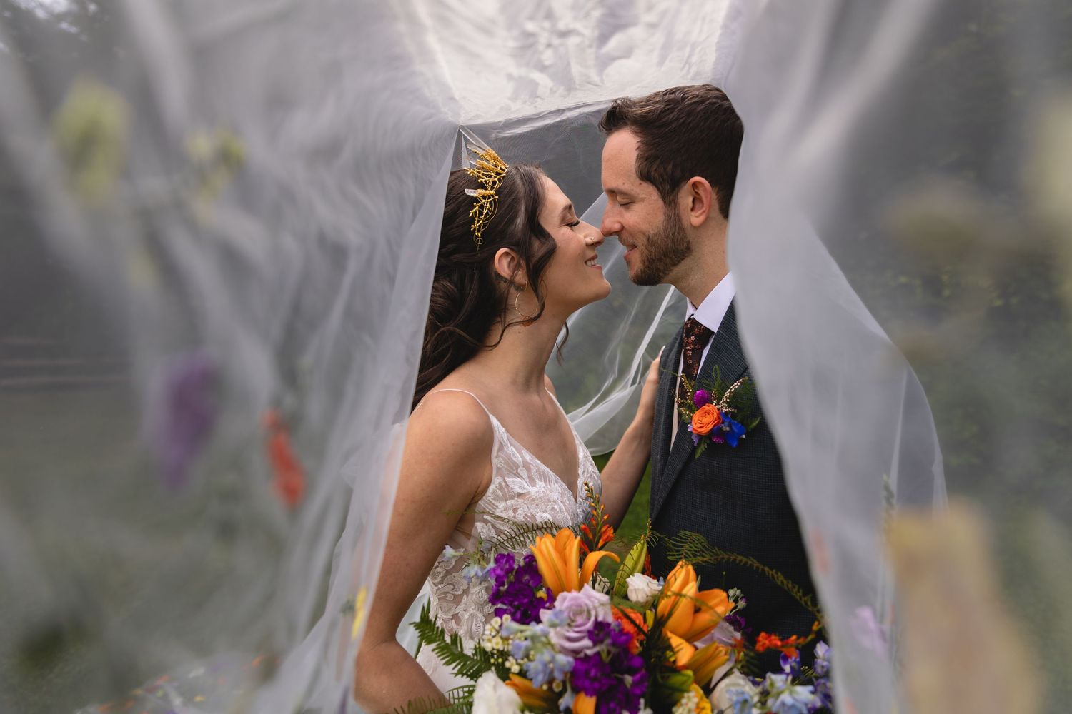 Artistic wedding portrait through sheer veil with vibrant floral bouquet.