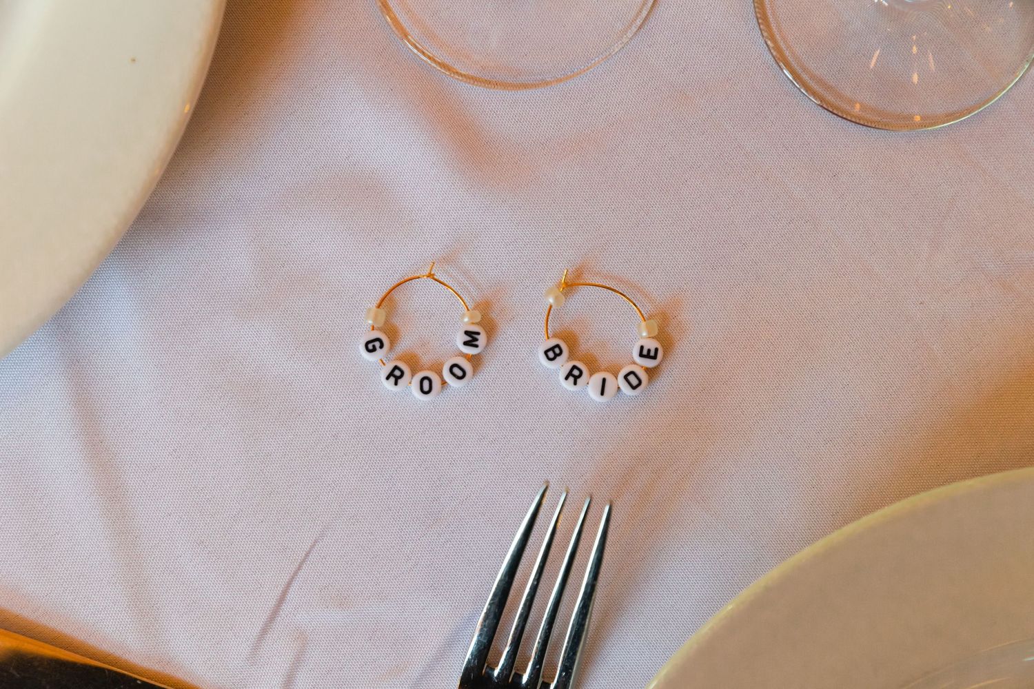 Delicate rose gold hoop earrings with small black accent beads displayed on white fabric near silverware.