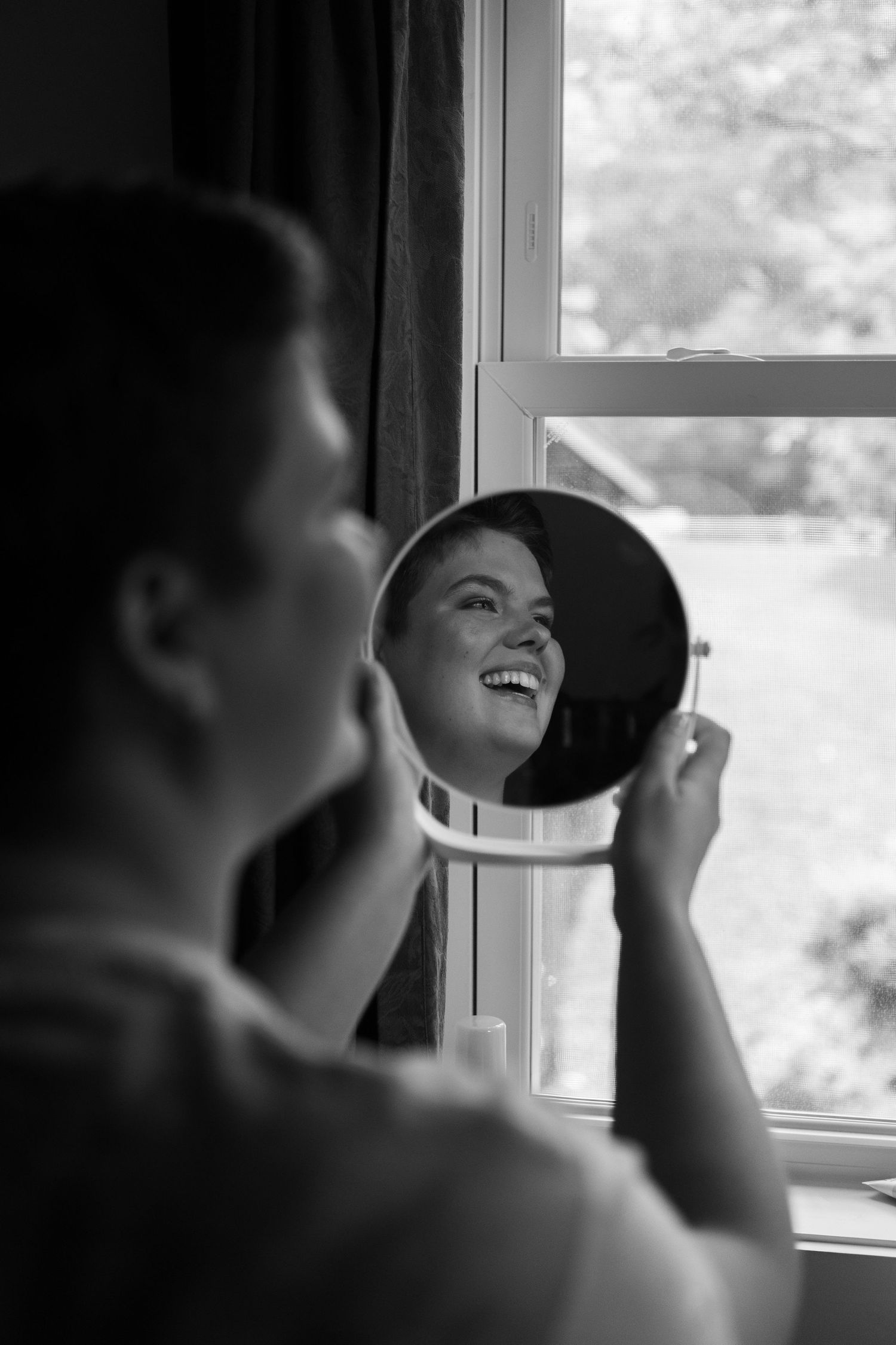 Black and white photo of joyful mirror reflection by window.