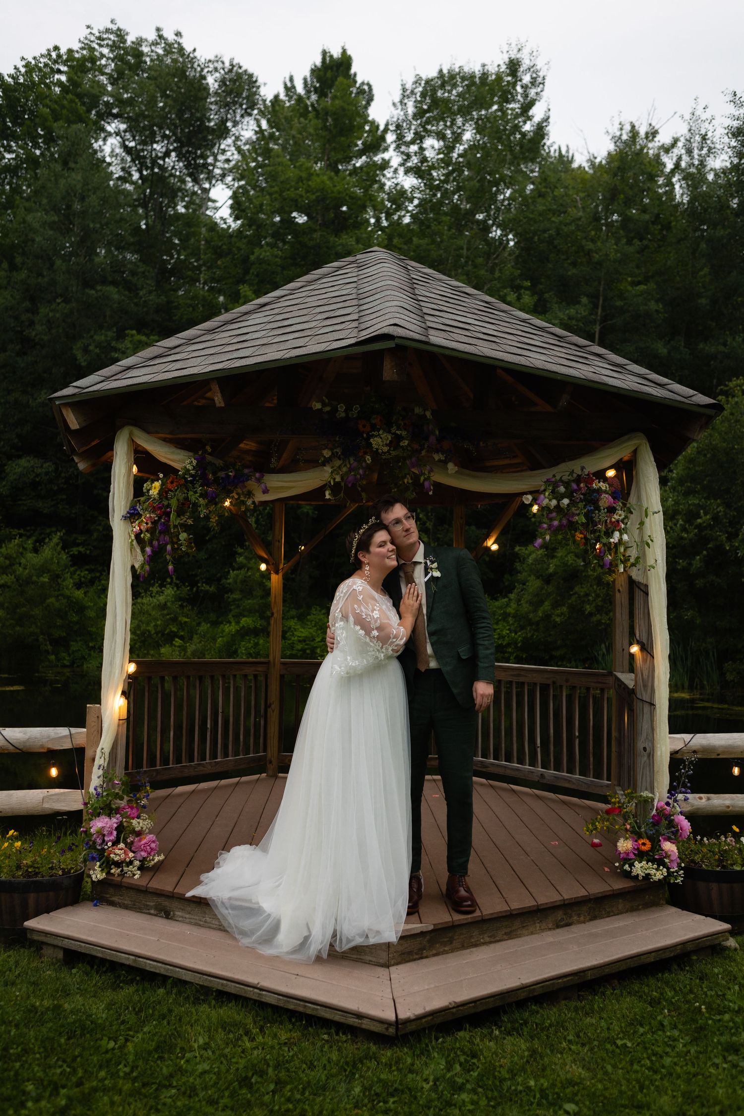 A decorated gazebo with string lights and floral arrangements serves as a romantic wedding backdrop.