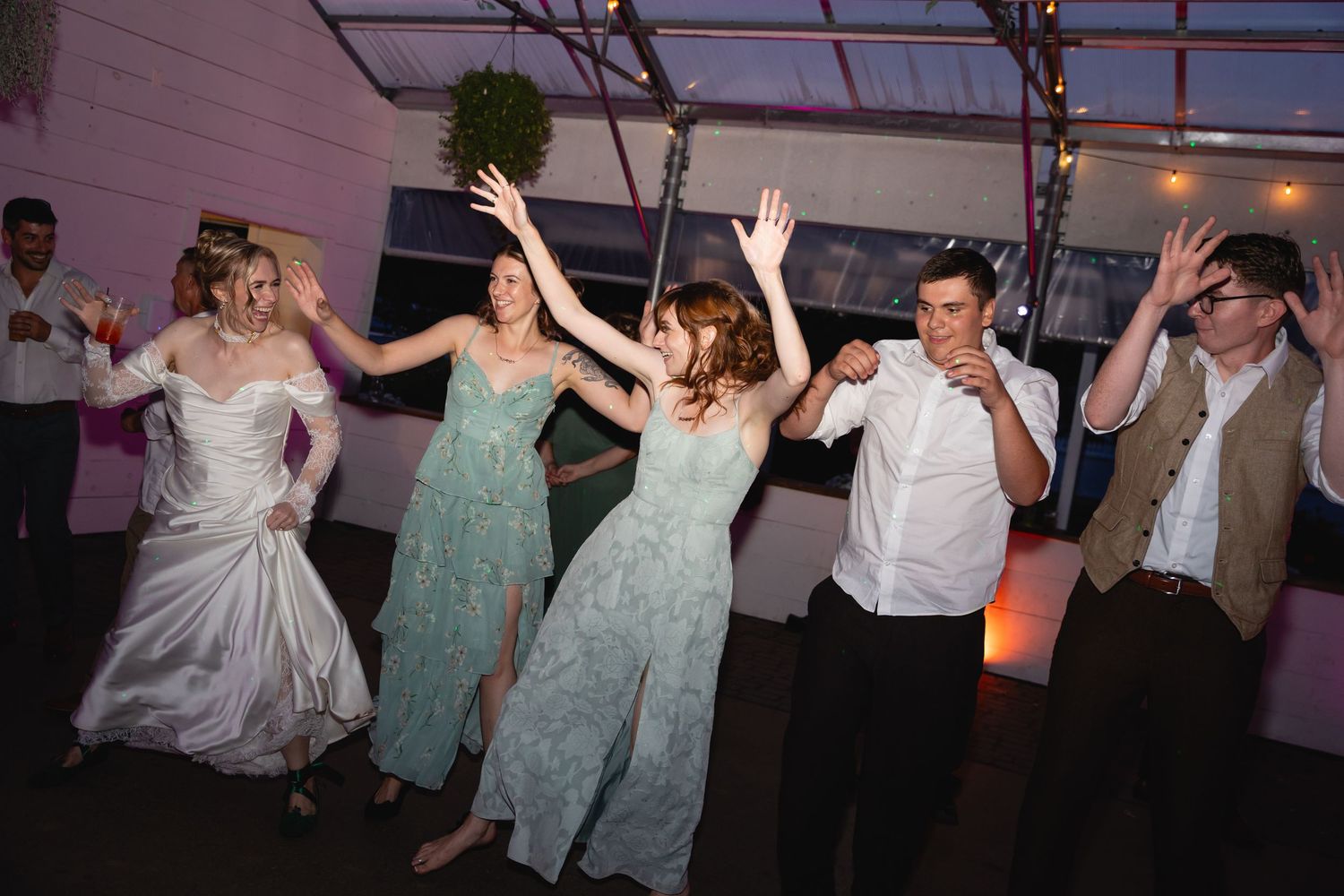Wedding party guests dance with their arms raised during an evening reception celebration.