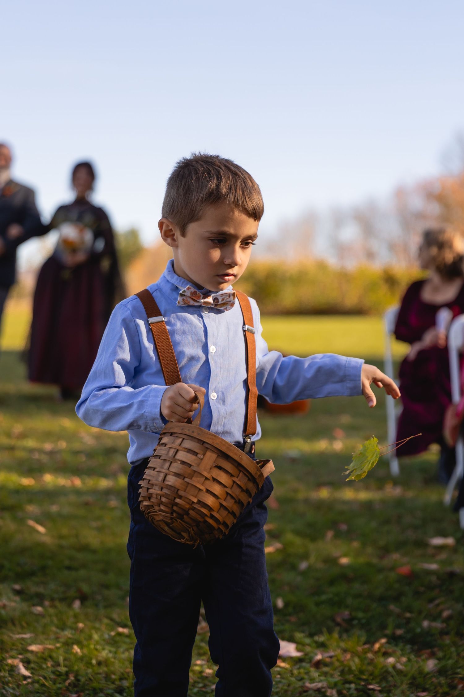 A young baseball player in a blue shirt and brown glove practices fielding drills on a grassy field in autumn.