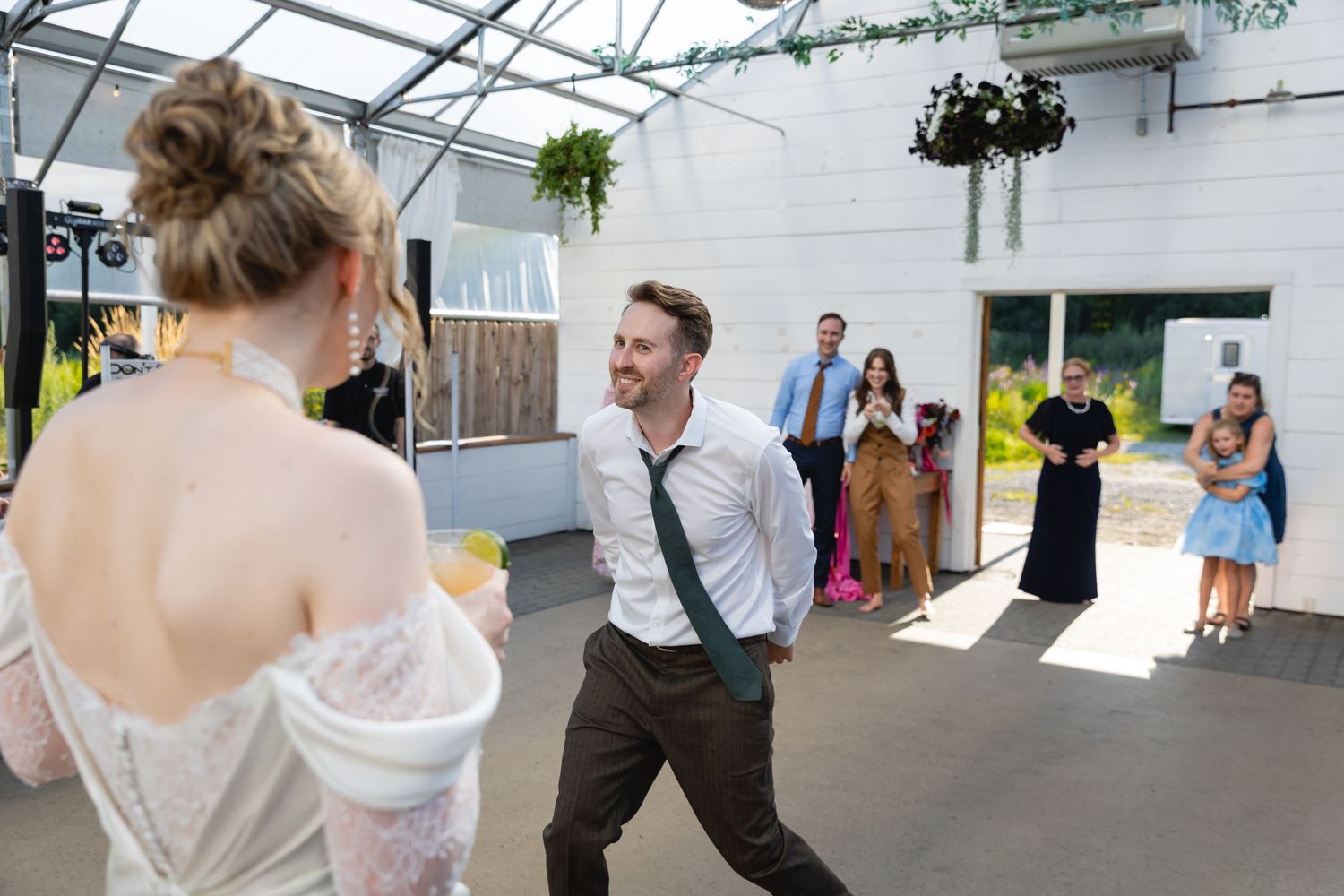 Wedding guests dance and celebrate together under a white tent during an outdoor reception celebration.