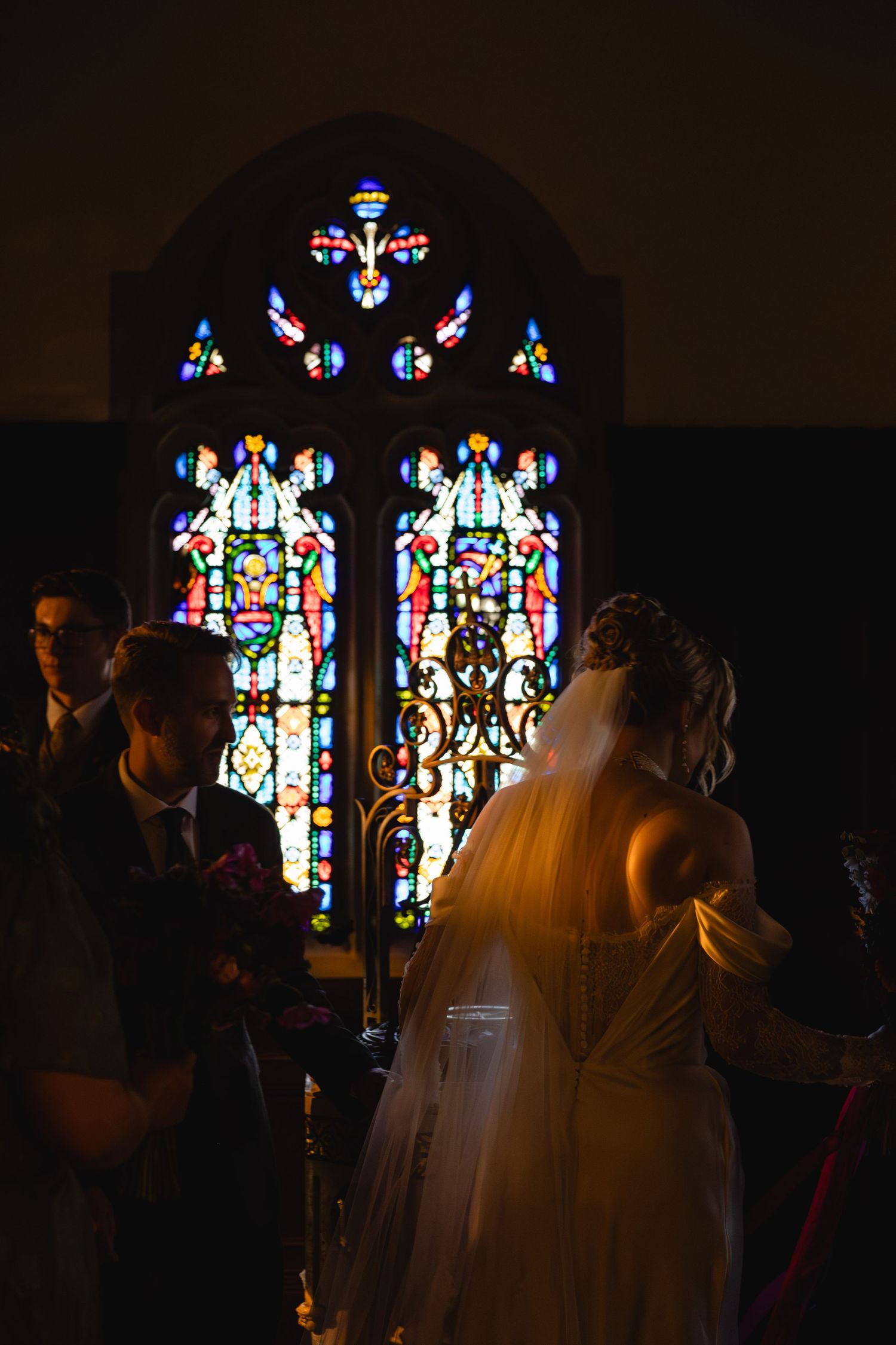 A silhouetted couple stands in front of a beautiful stained glass church window during their wedding ceremony.