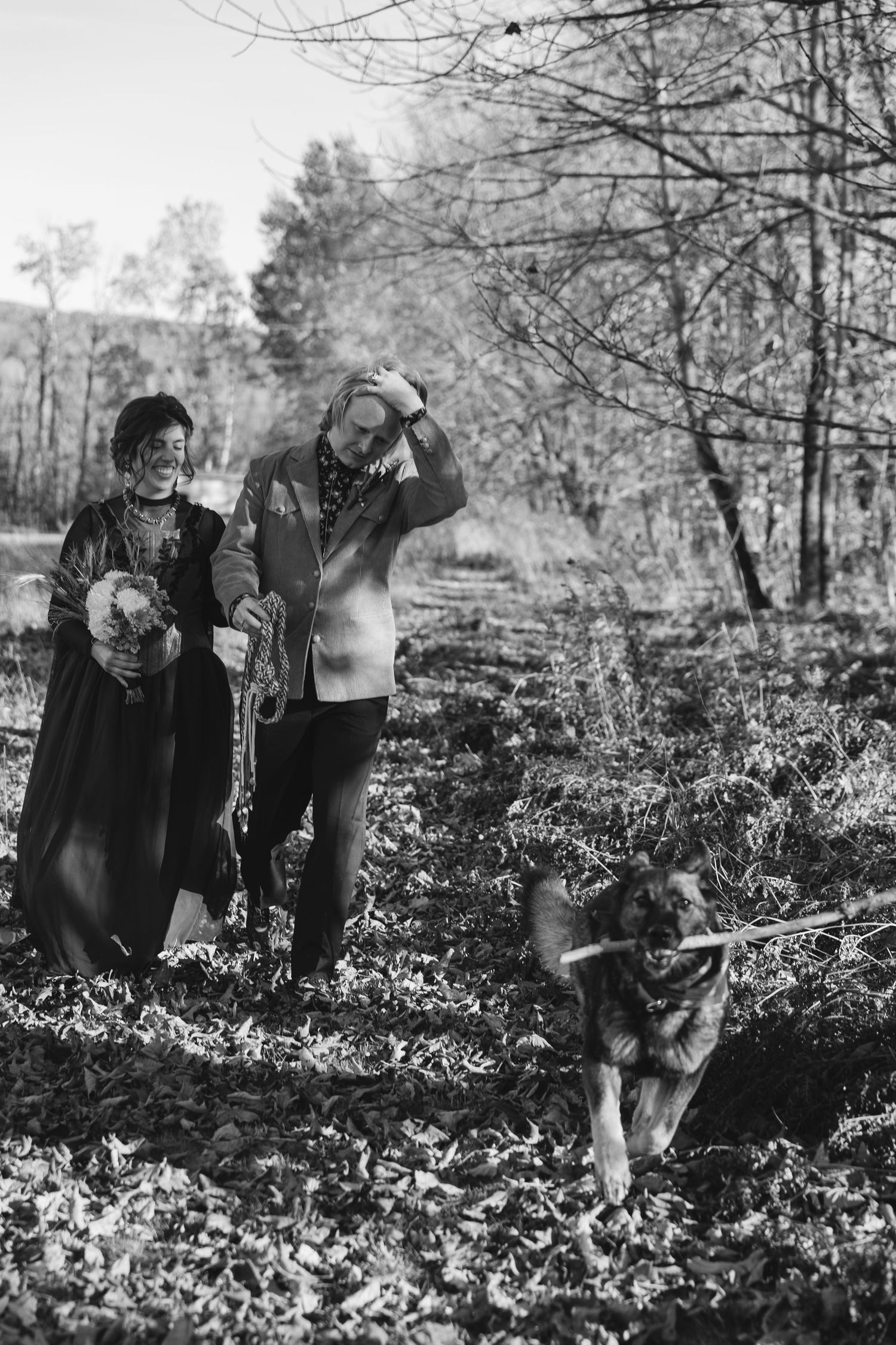 A group of people stand together in a wooded area among low-growing plants and bare winter trees.