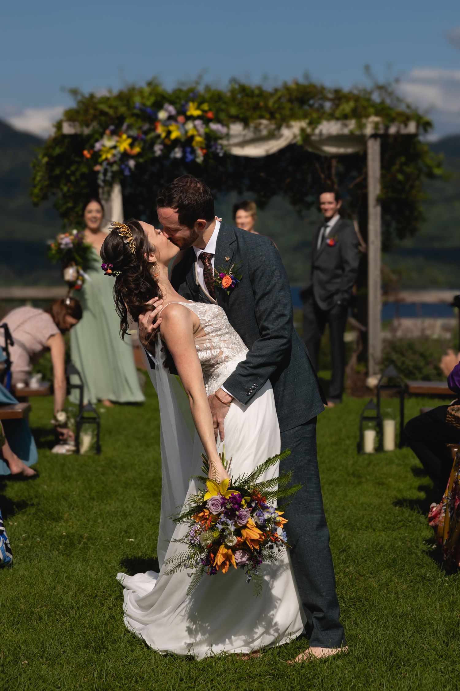 A romantic wedding kiss under a floral archway during an outdoor ceremony.