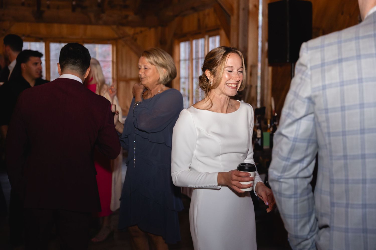 Candid party scene at a rustic indoor venue with people mingling and socializing near wooden walls.