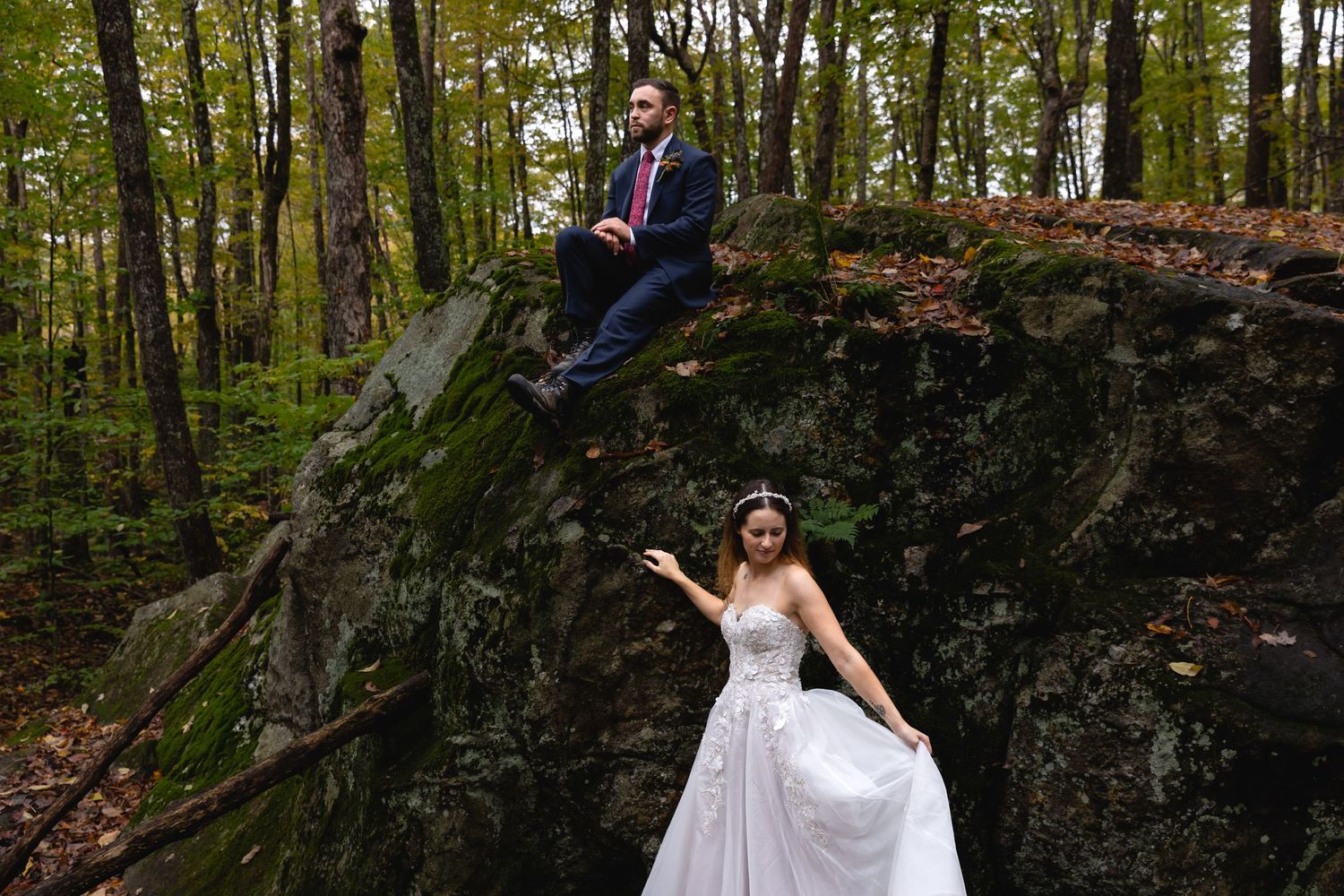 Creative wedding photo with couple posing playfully on different levels of a rocky forest outcrop.