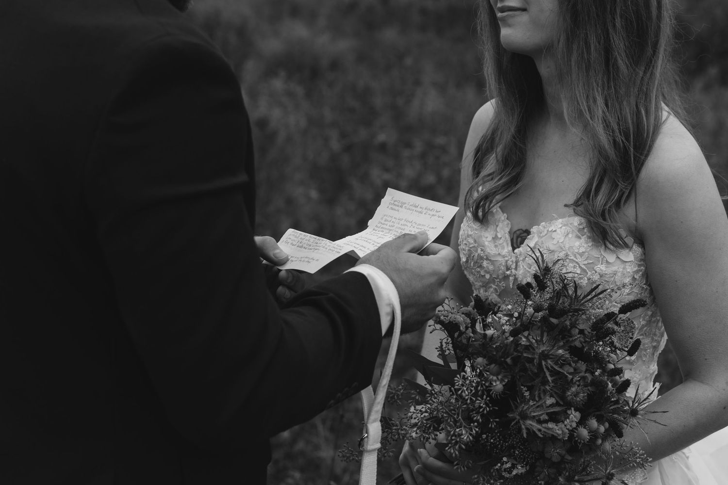 A black and white close-up of wedding vows being exchanged with a bouquet in view.