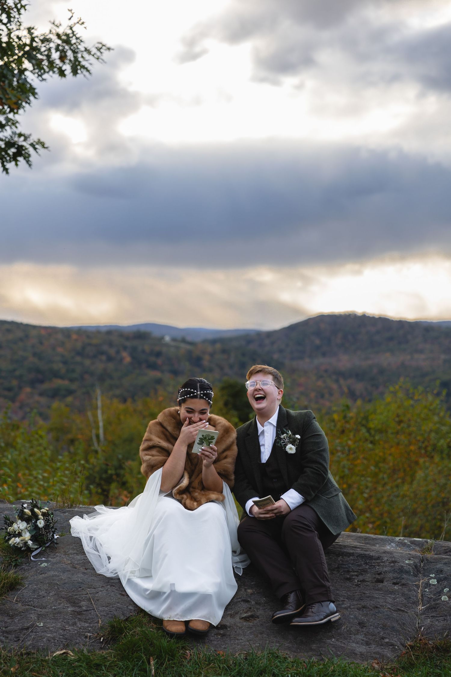Newlyweds sharing a joyful moment on a rocky overlook with mountain views at sunset.