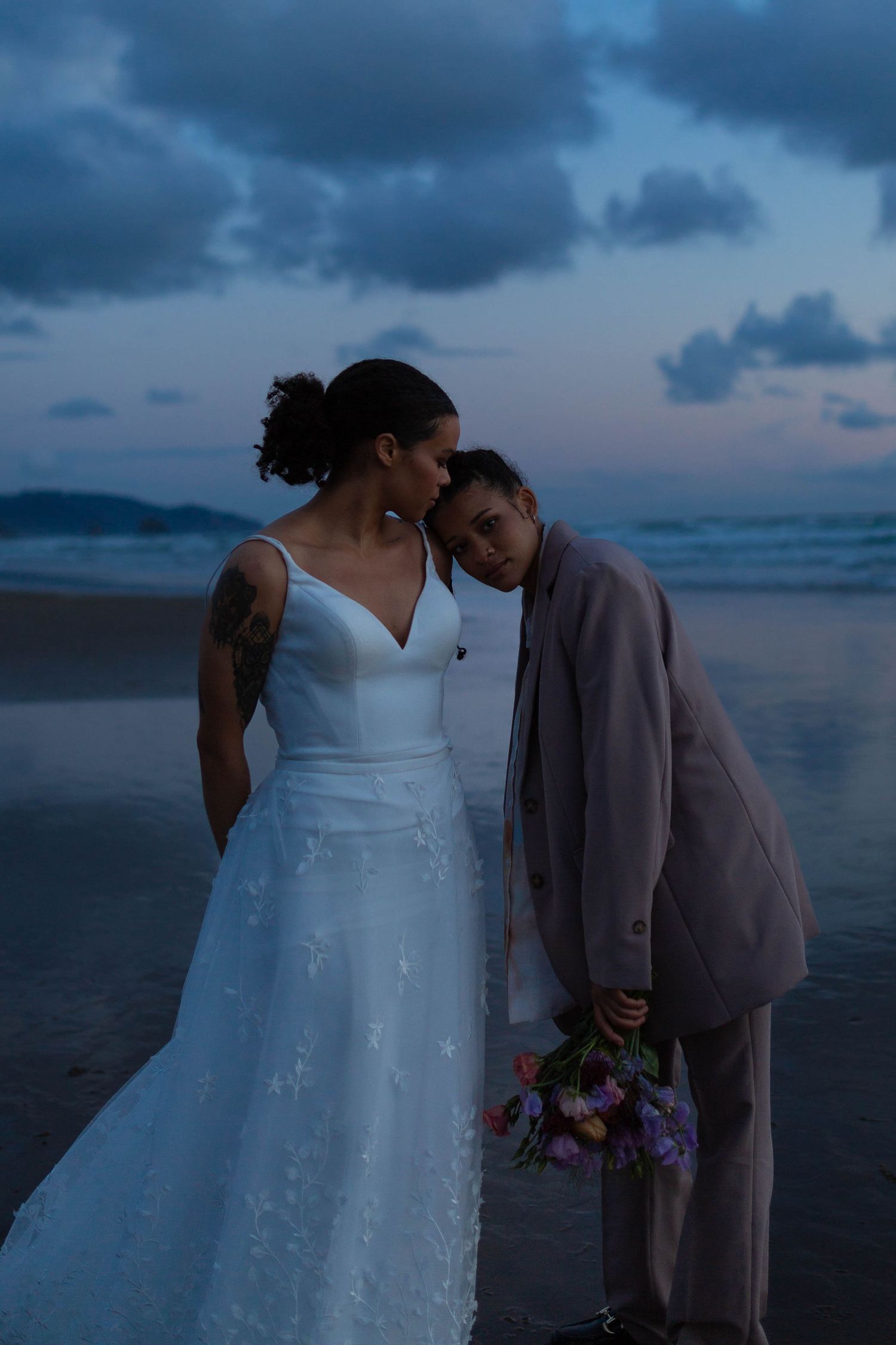 A tender moment between a couple on a moody beach at dusk.