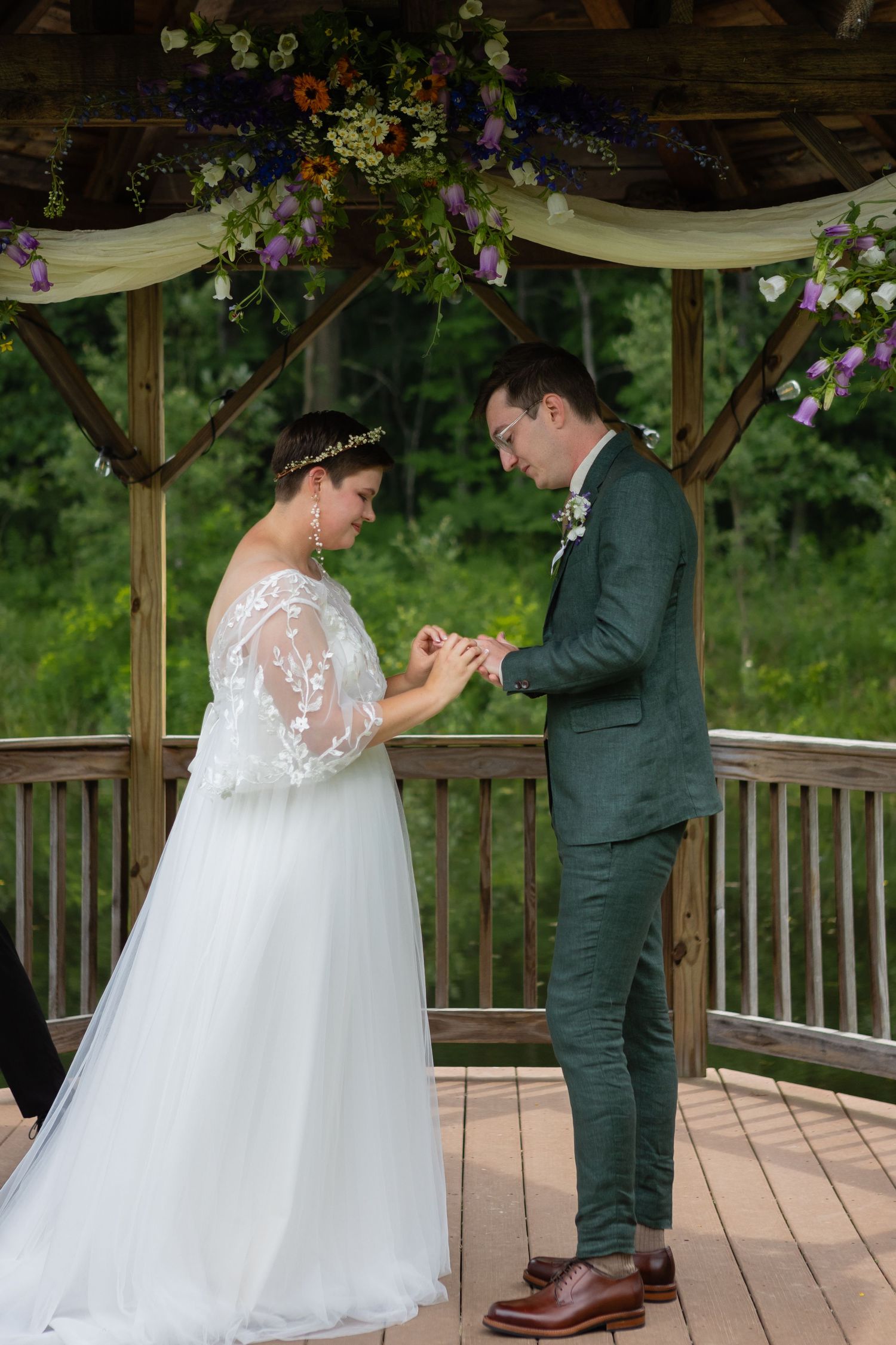 Ring exchange during outdoor gazebo wedding ceremony with floral and fabric decorations.