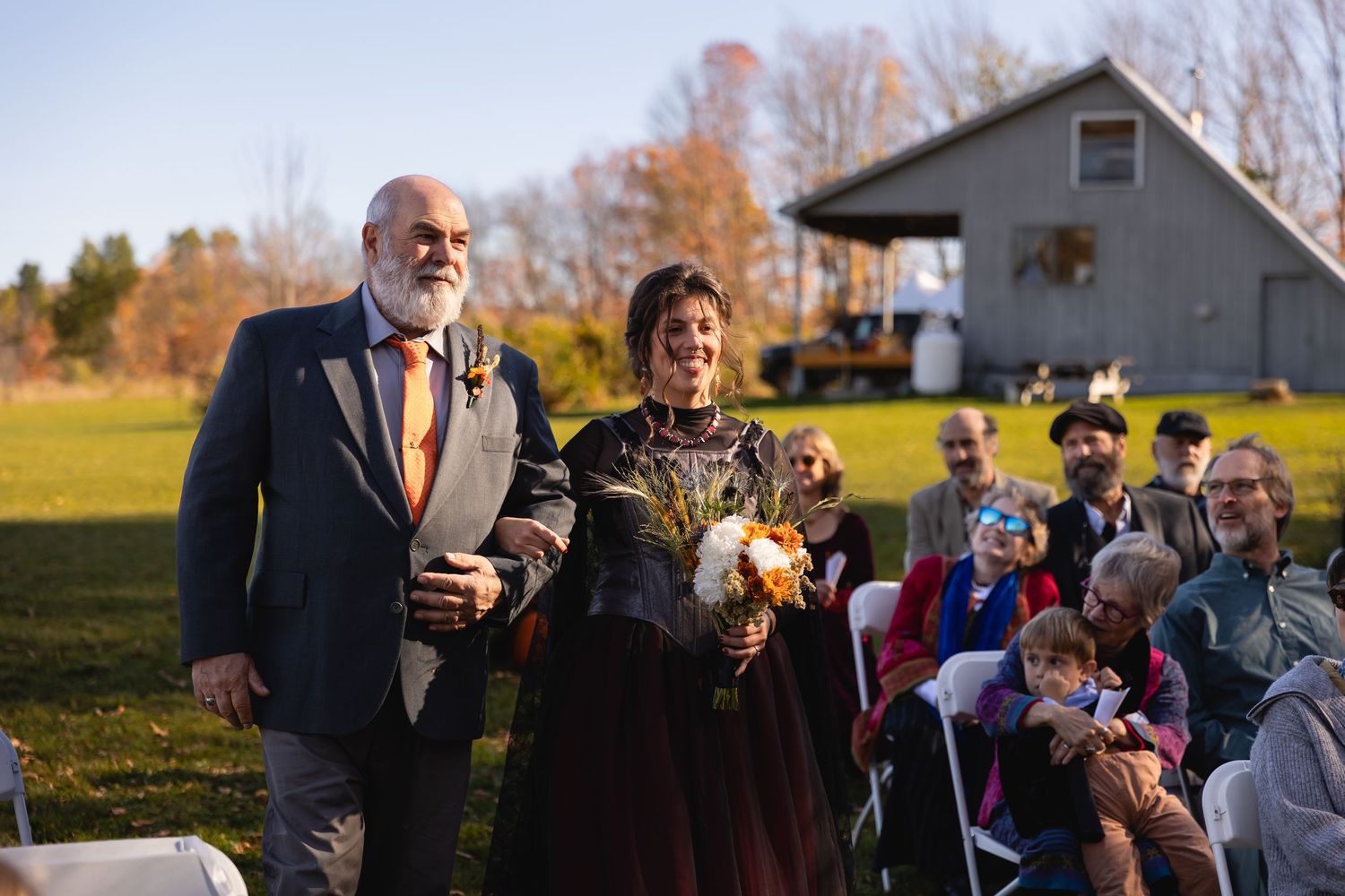 A group gathers outdoors on an autumn afternoon during a social event with golden sunlight in the background.