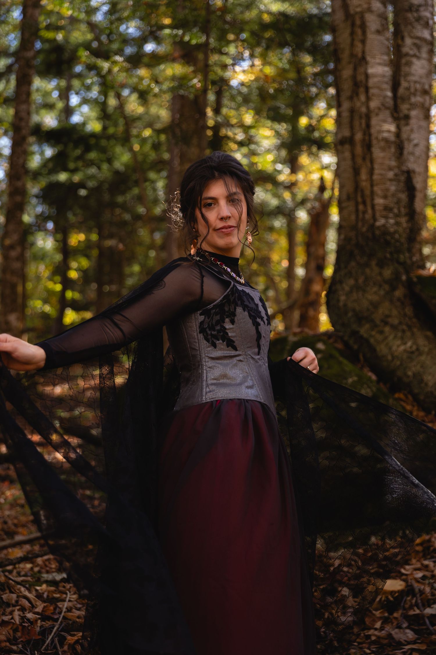 A person in a dark sheer top and burgundy skirt twirls gracefully through a sunlit autumn forest.