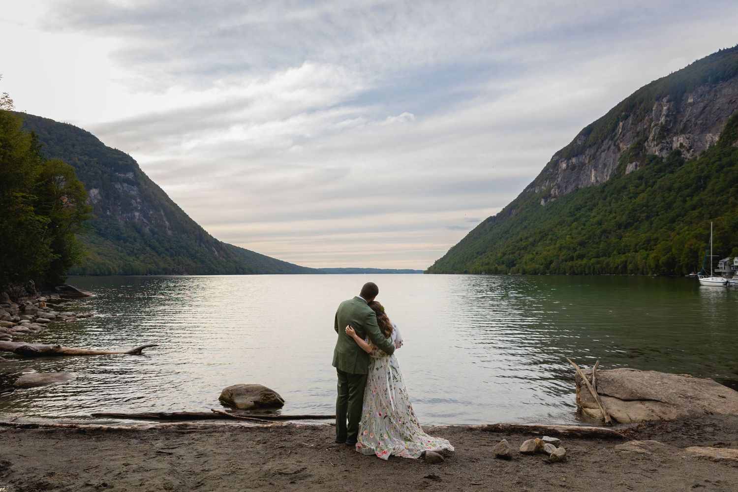 A scenic mountain lake view with dramatic cliffs and cloudy skies as backdrop for a wedding photo.