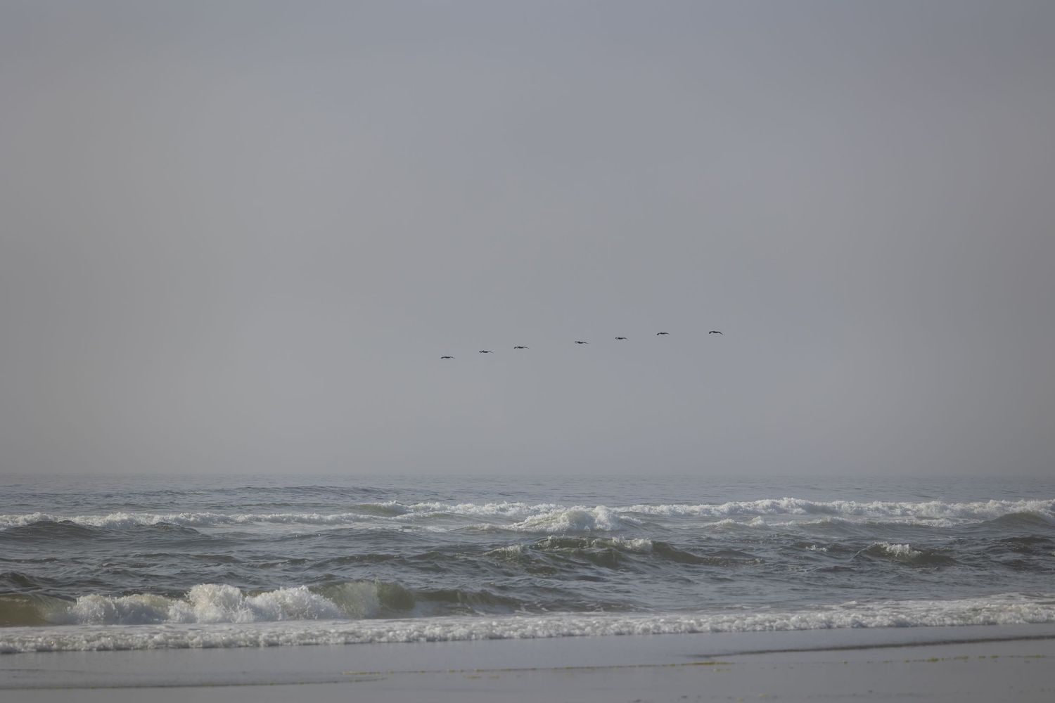 Stormy ocean waves crash against the shore on a cloudy day with rough seas and white foam in the surf.