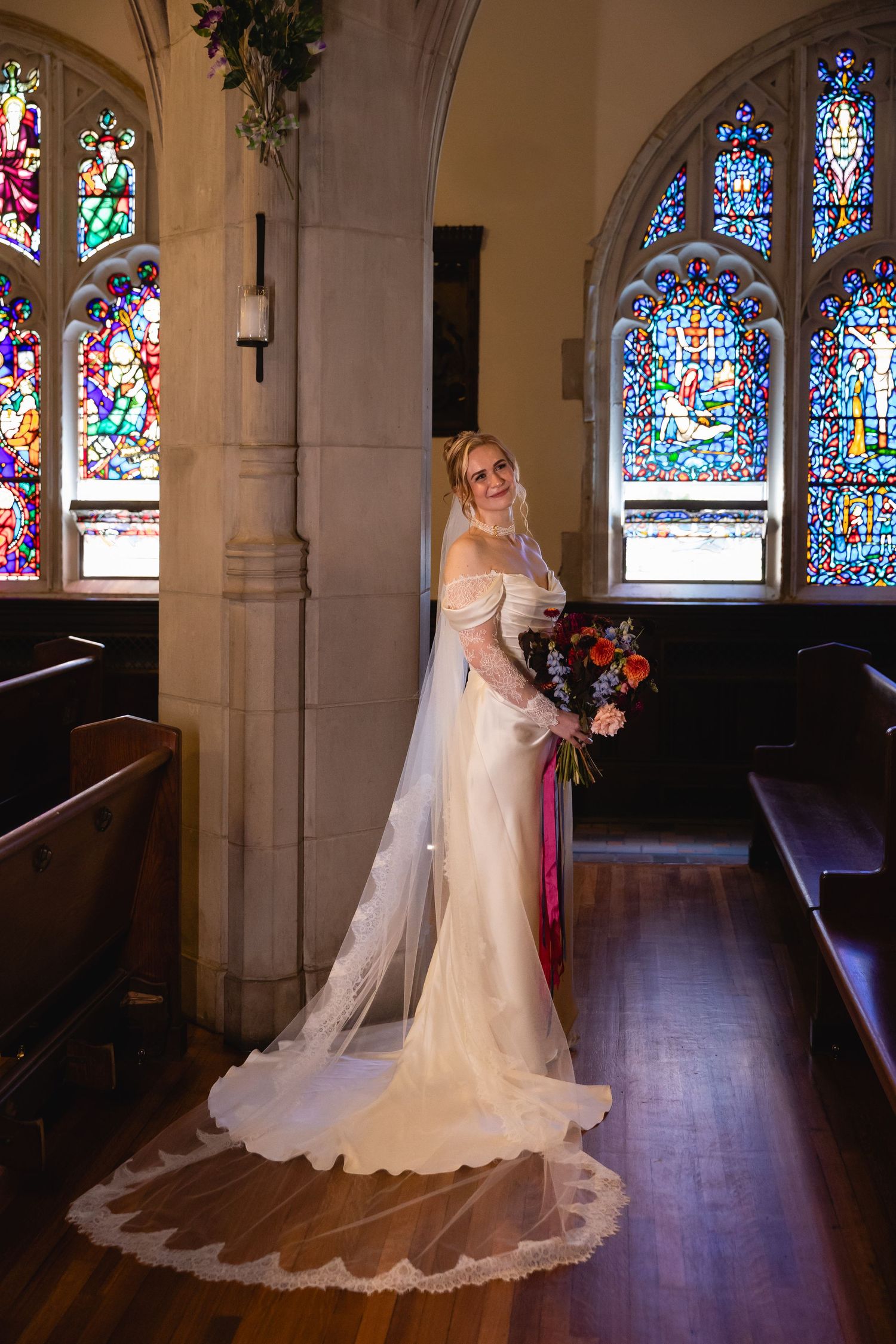 A bride in a flowing white gown poses in a church sanctuary with beautiful stained glass windows and hardwood floors.