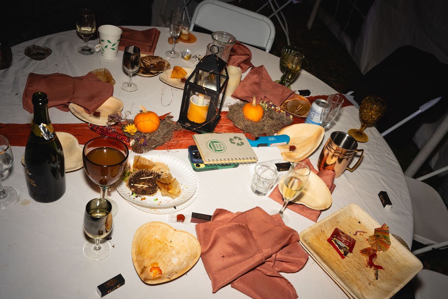 A dimly lit dining table with scattered plates of food, drinks, and a lantern creating an intimate dinner atmosphere.